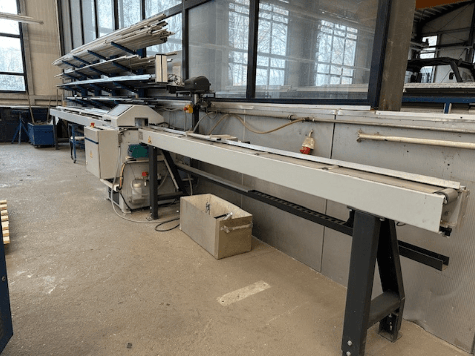 SCHÜCO PGS kružna pila za metal u radionici, bočni pogled s podesivim postoljem za rezanje i policom metalnih profila iznad.