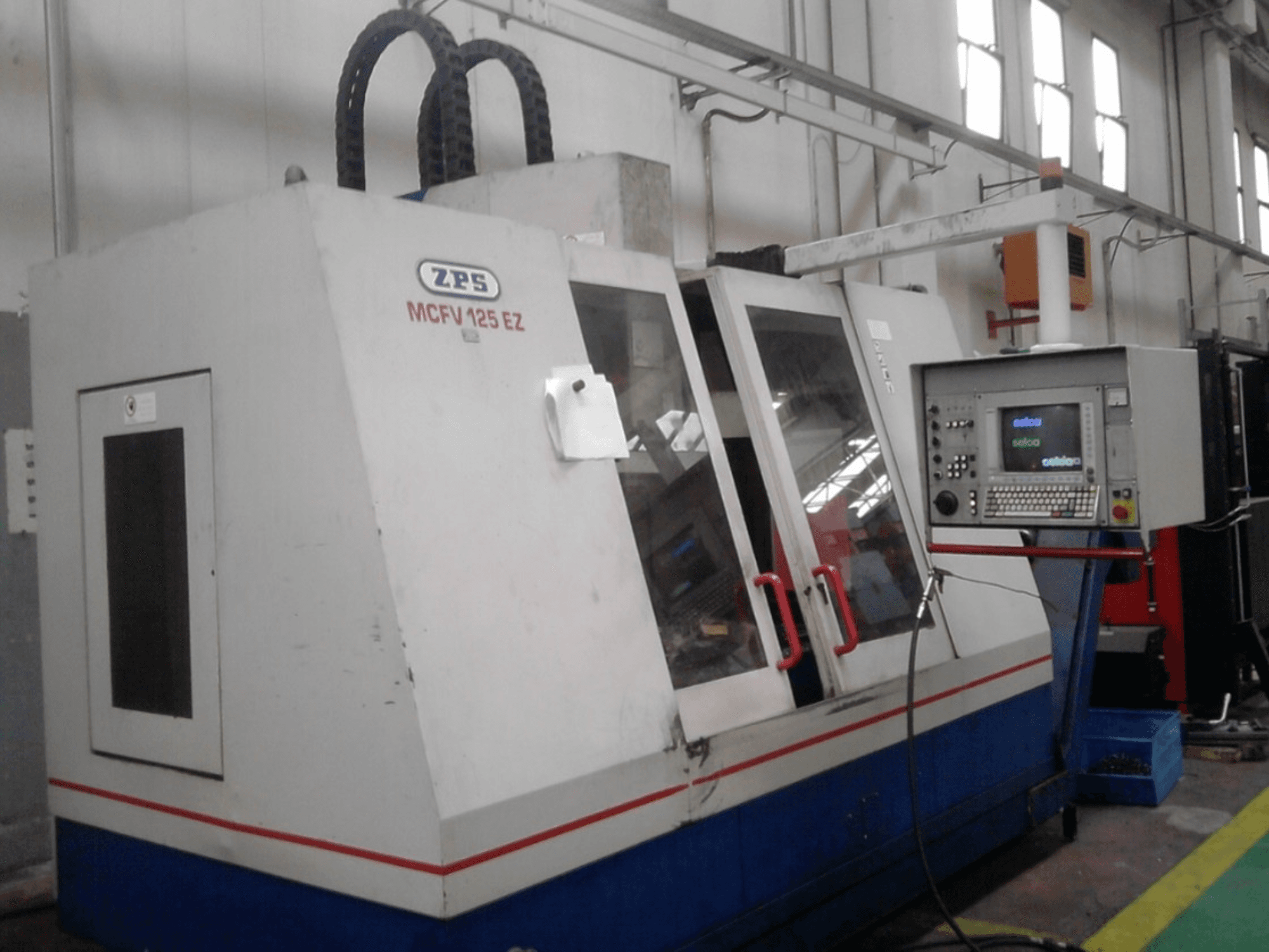 ZPS MCFV 125 EZ CNC stroj, prednji pogled s upravljačkom pločom i crvenim ručkama, u radioničkom okruženju s vidljivim crijevima.