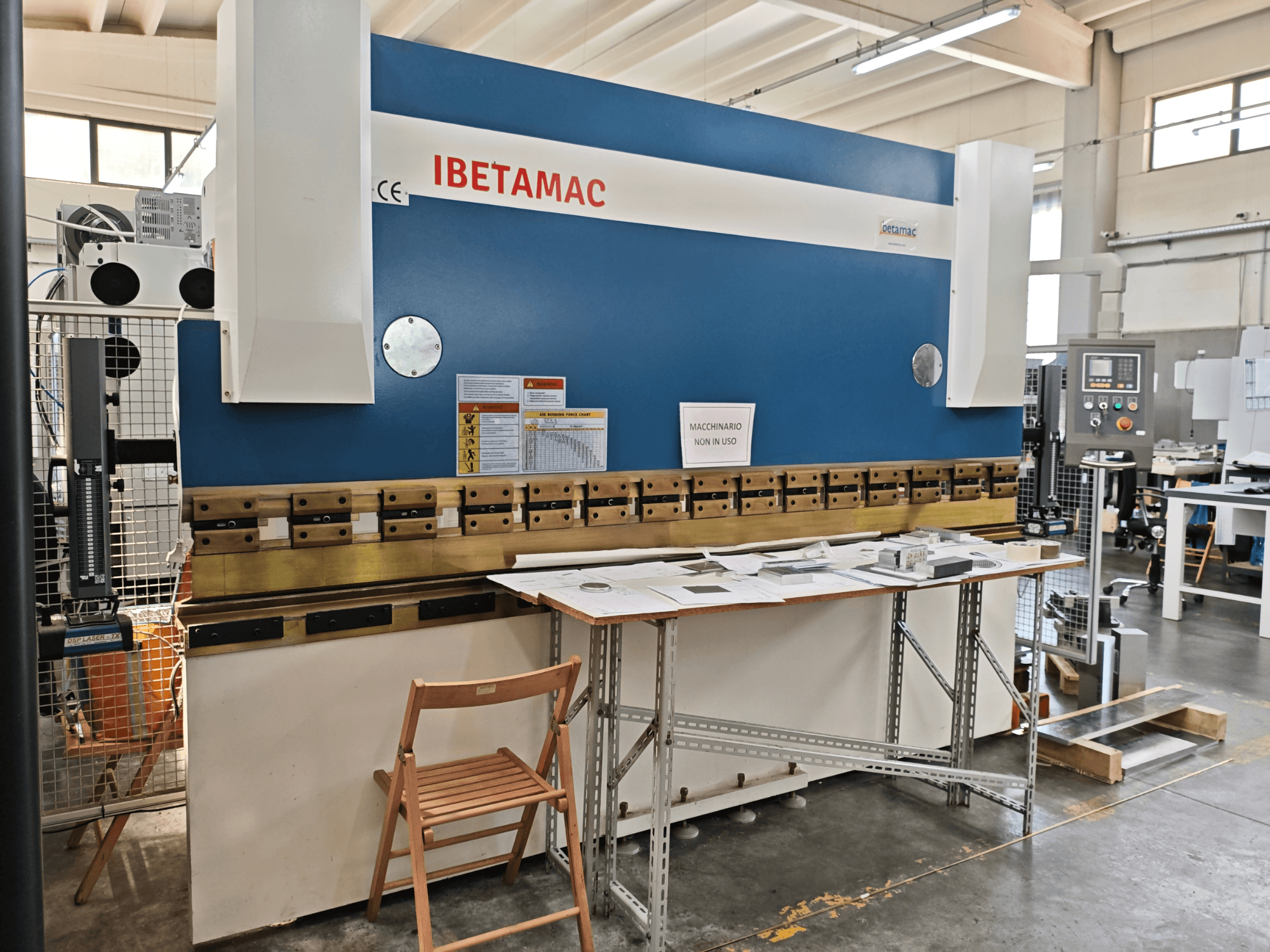 IBETAMAC 3200 100T preša za savijanje u radionici, bočni pogled koji prikazuje upravljačku ploču, radno područje i sigurnosne napomene.