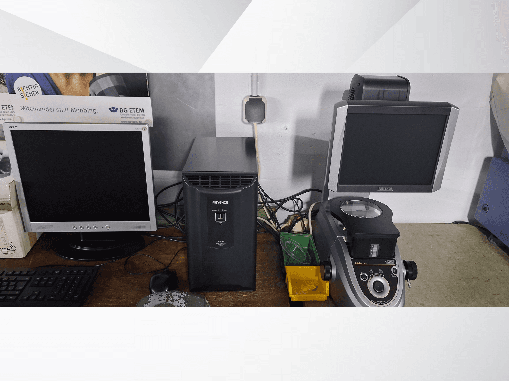 Dva računalna monitora, jedan Acer i jedan Keyence, pored crnog uređaja i mikroskopa, gledano sprijeda.