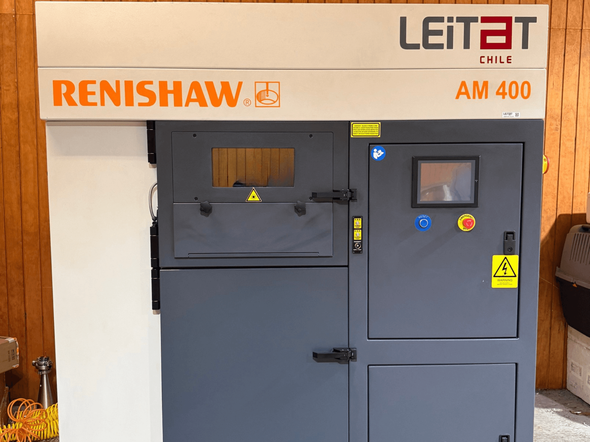 Prednji pogled na metalni 3D printer RENISHAW AM400, s upravljačkom pločom, naljepnicama s upozorenjima i pristupom za održavanje.