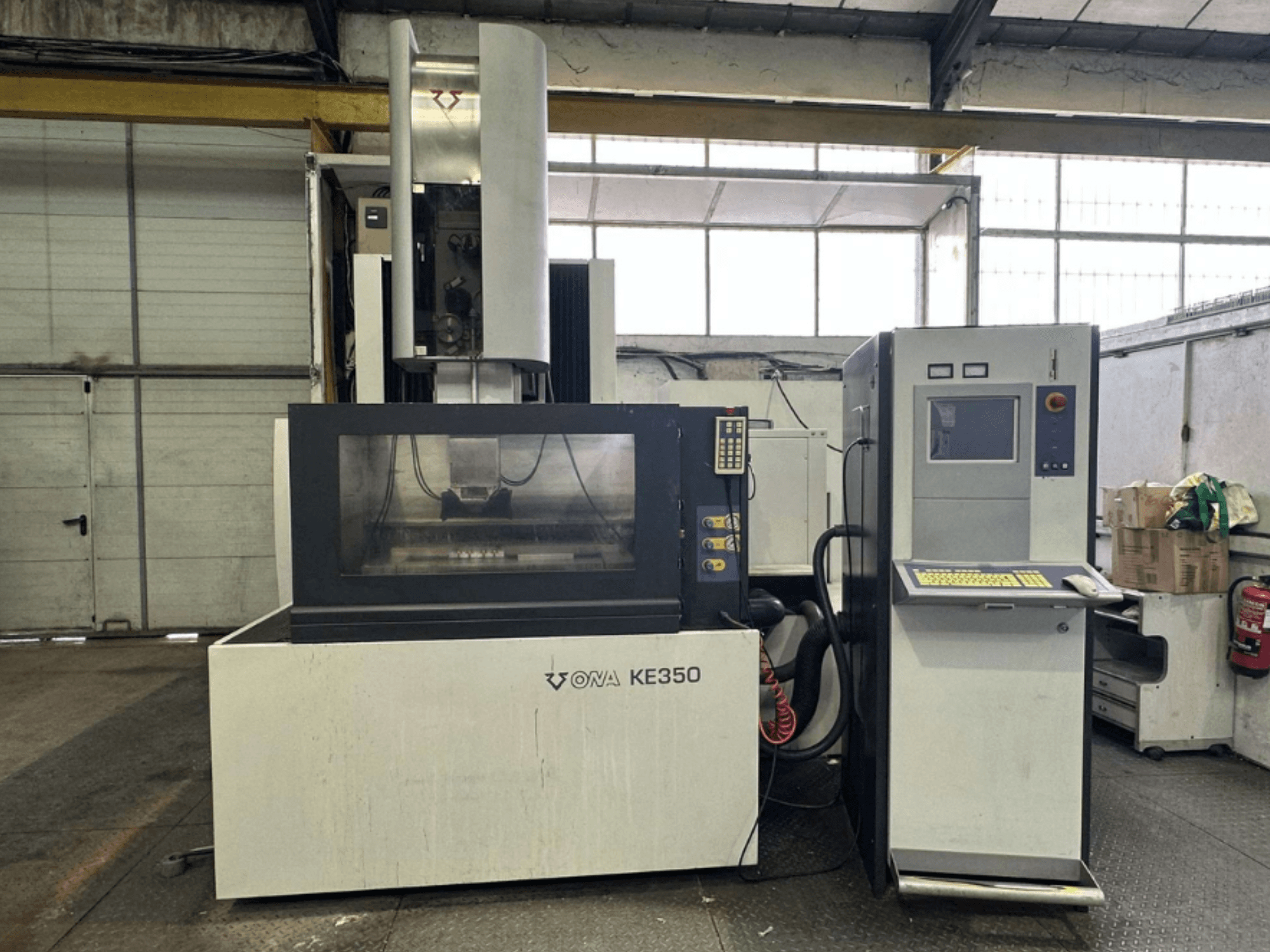 Prednji pogled na CNC stroj ONA KE350 s upravljačkom pločom, zaslonom i raznim gumbima, smješten u industrijskom okruženju.