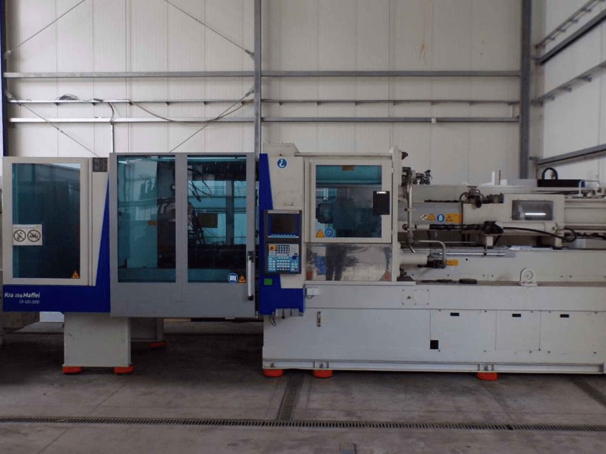 Stroj za brizganje plastike KraussMaffei, bočni pogled, ima upravljačku ploču i sigurnosne indikatore, vidljive u tvorničkom okruženju.