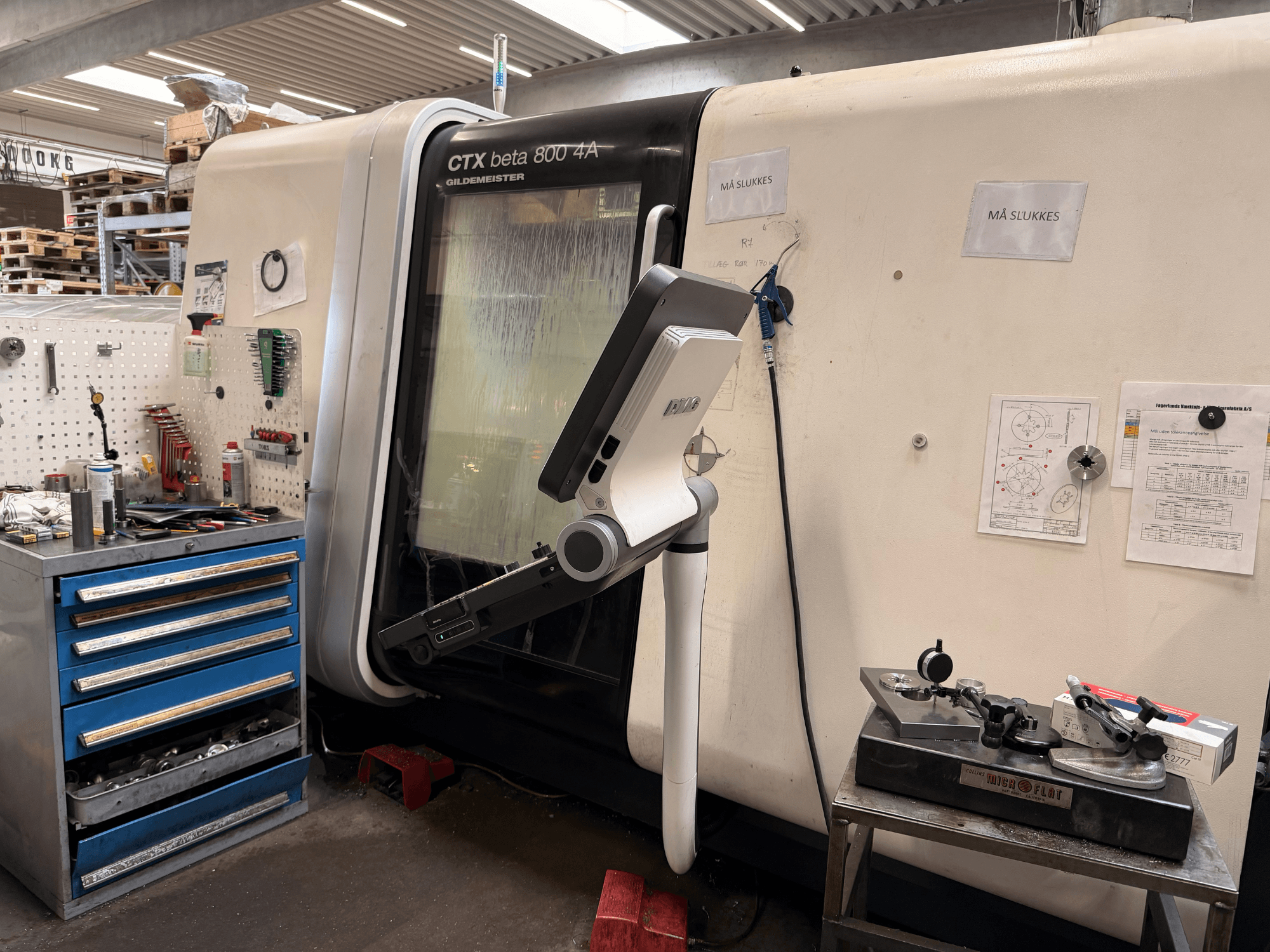 Vertikalni tokarski stroj DMG MORI CTX Beta 800 4a u radionici, s upravljačkom rukom i tehničkom dokumentacijom u blizini.