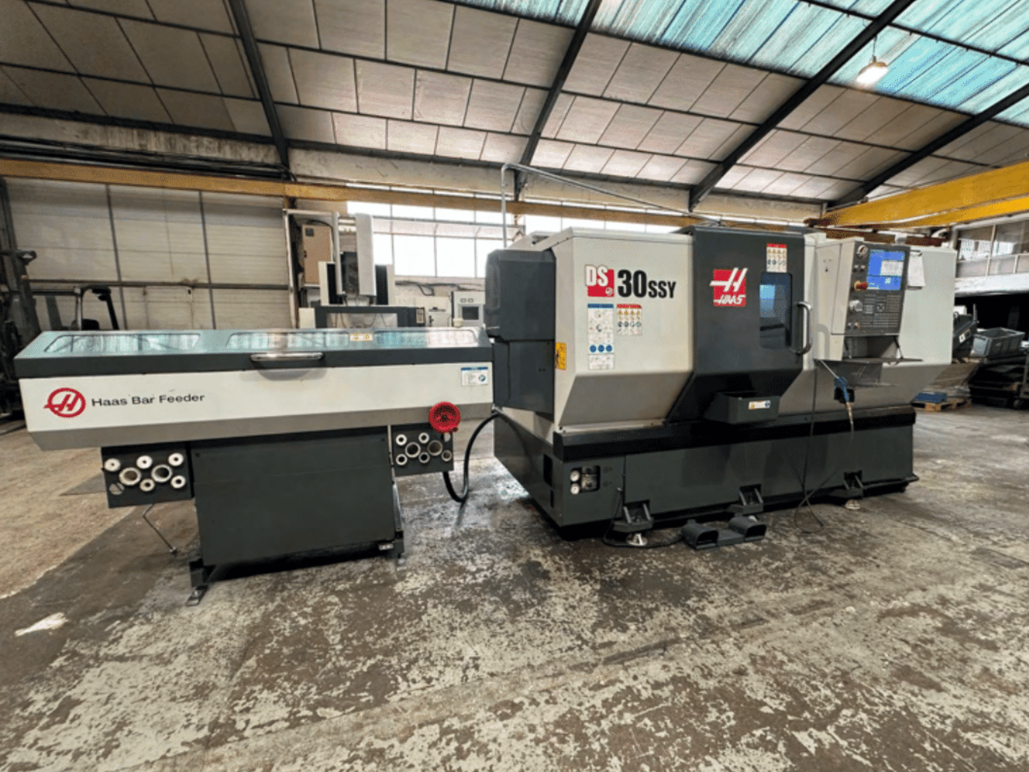 Haas DS-30SSY CNC tokarilica s Haas uvlakačem šipki, bočni pogled s upravljačkom pločom i mehanizmom za uvlačenje u radioničkom okruženju.