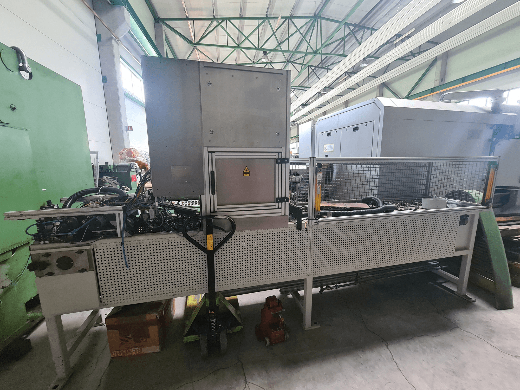 Industrijski strojevi s metalnim okvirom, crijevima i upravljačkom pločom, gledani sa strane u tvorničkom okruženju.