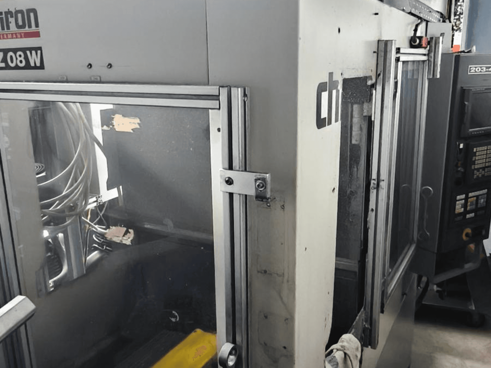 Vertikalni obradni centar CHIRON FZ 08 W, prednji pogled s upravljačkom pločom i djelomično otvorenim vratima, s vidljivim unutarnjim komponentama.