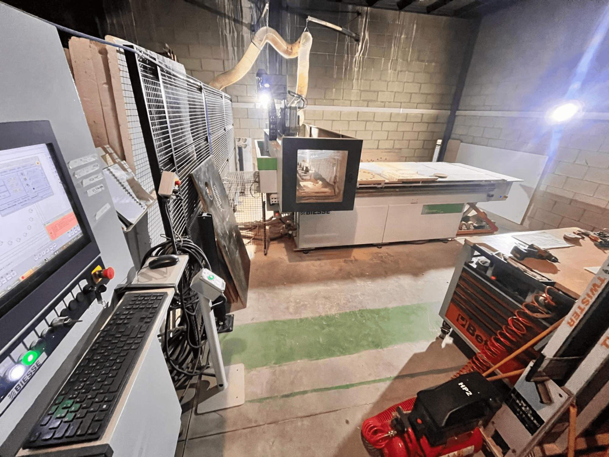 Biesse CNC stroj u radionici, bočni pogled koji prikazuje upravljačku ploču, usisavanje prašine, alate i razne materijale na stolu.