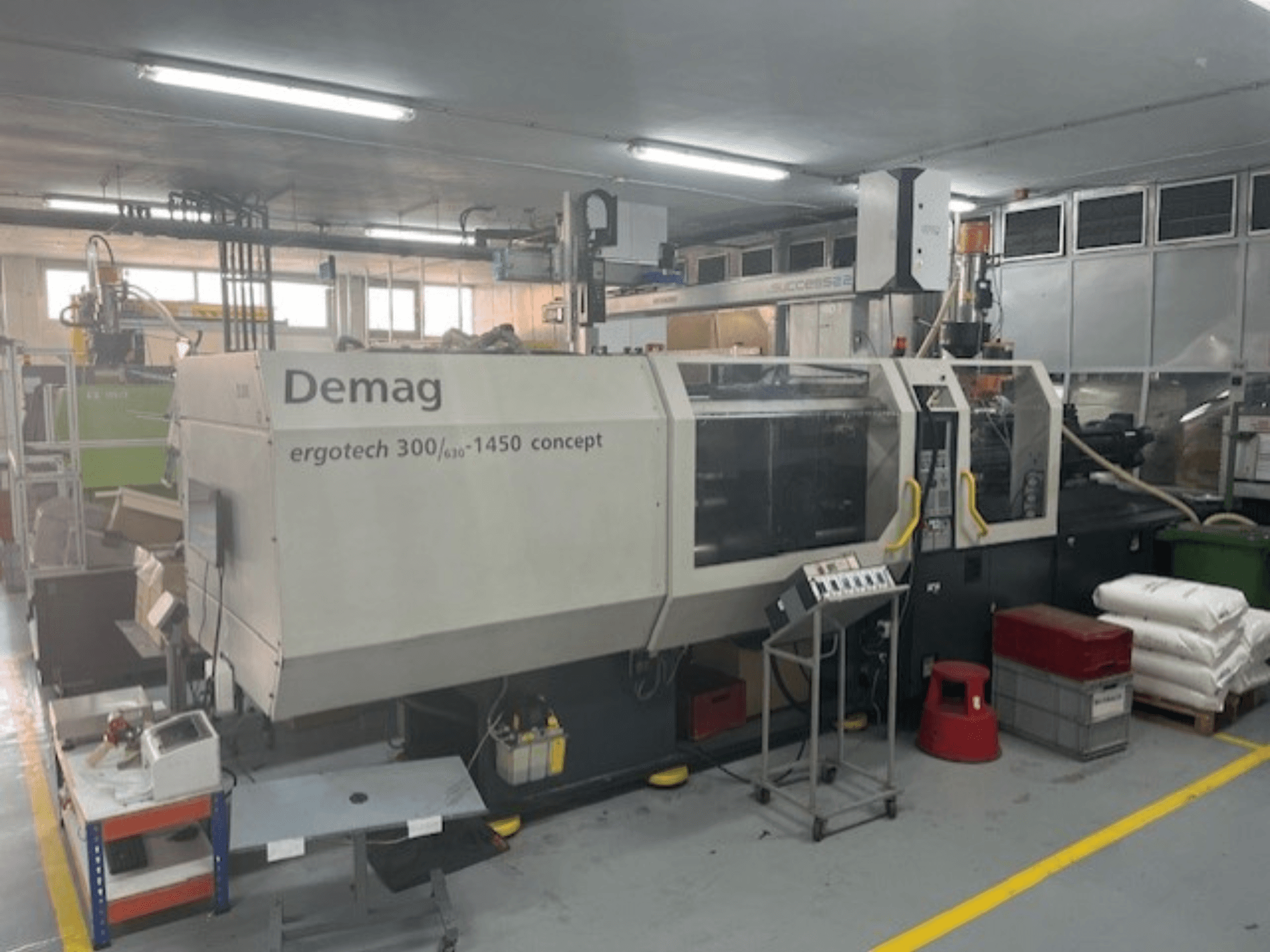 Demag ERGOTECH CONCEPT 3000-1450 hidraulični stroj za brizganje plastike, pogled sprijeda, s operativnim kontrolama i materijalima u blizini.