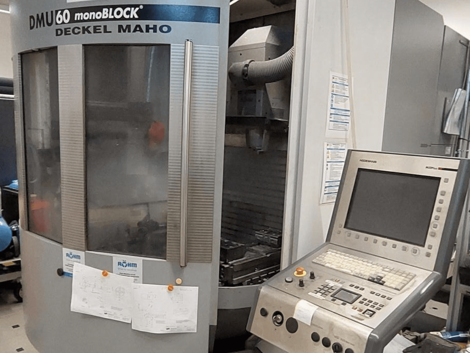 DMU 60 monoBLOCK tvrtke Deckel Maho, prednji pogled na CNC glodalicu s priloženom upravljačkom pločom i tehničkim crtežima.