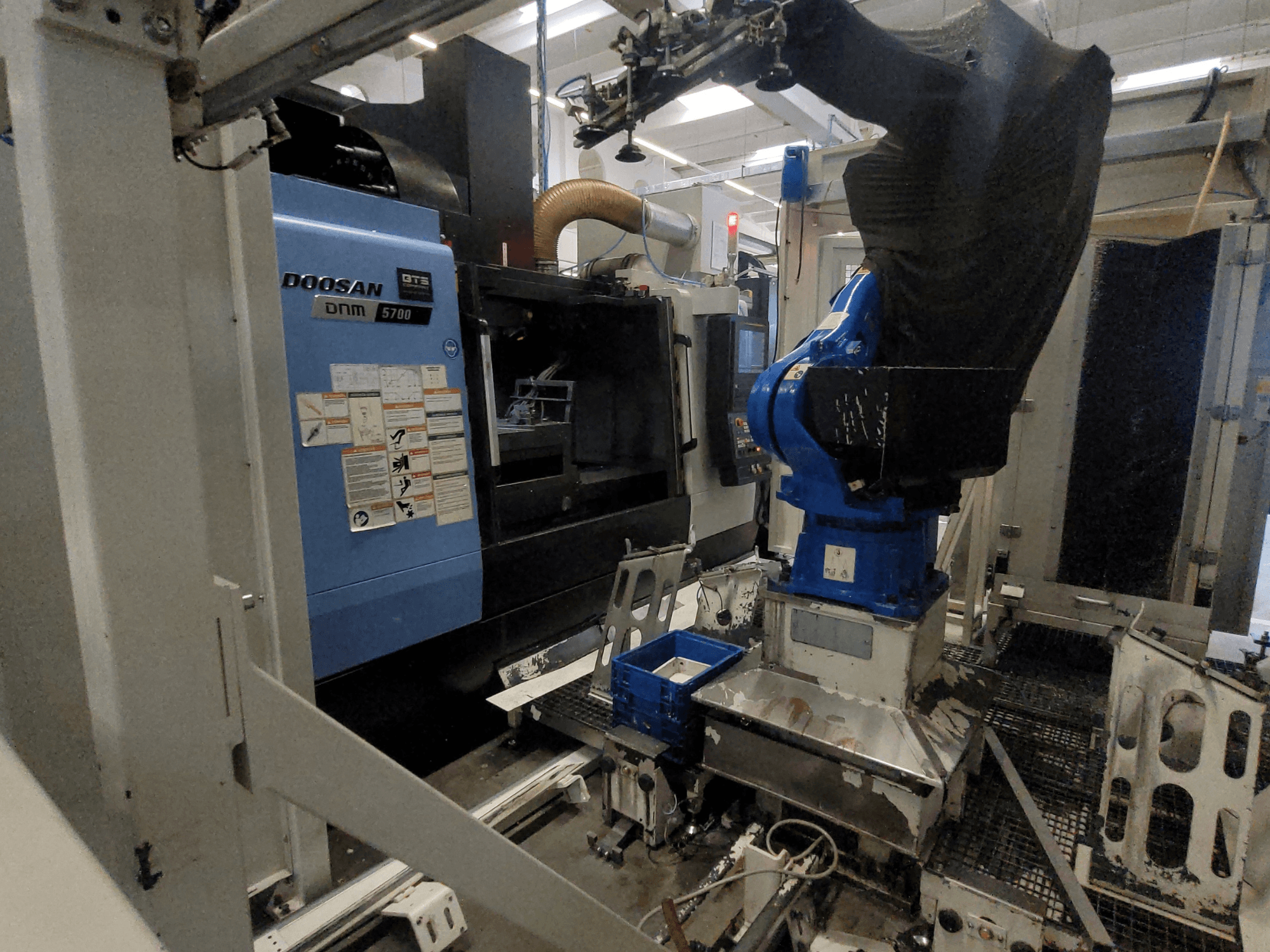 Vertikalni obradni centar DOOSAN DNM 5700 u tvorničkom okruženju, s prikazom prednje strane i integracije robotske ruke.