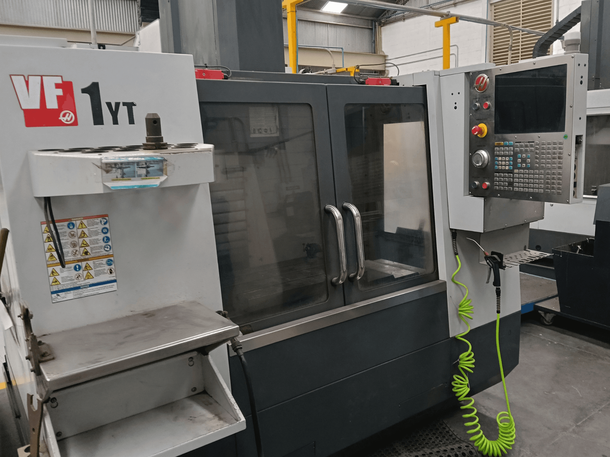 Vertikalni obradni centar HAAS VF-1YT-2, prednji pogled, prikazuje upravljačku ploču, držač alata, sigurnosne naljepnice i područje obrade.