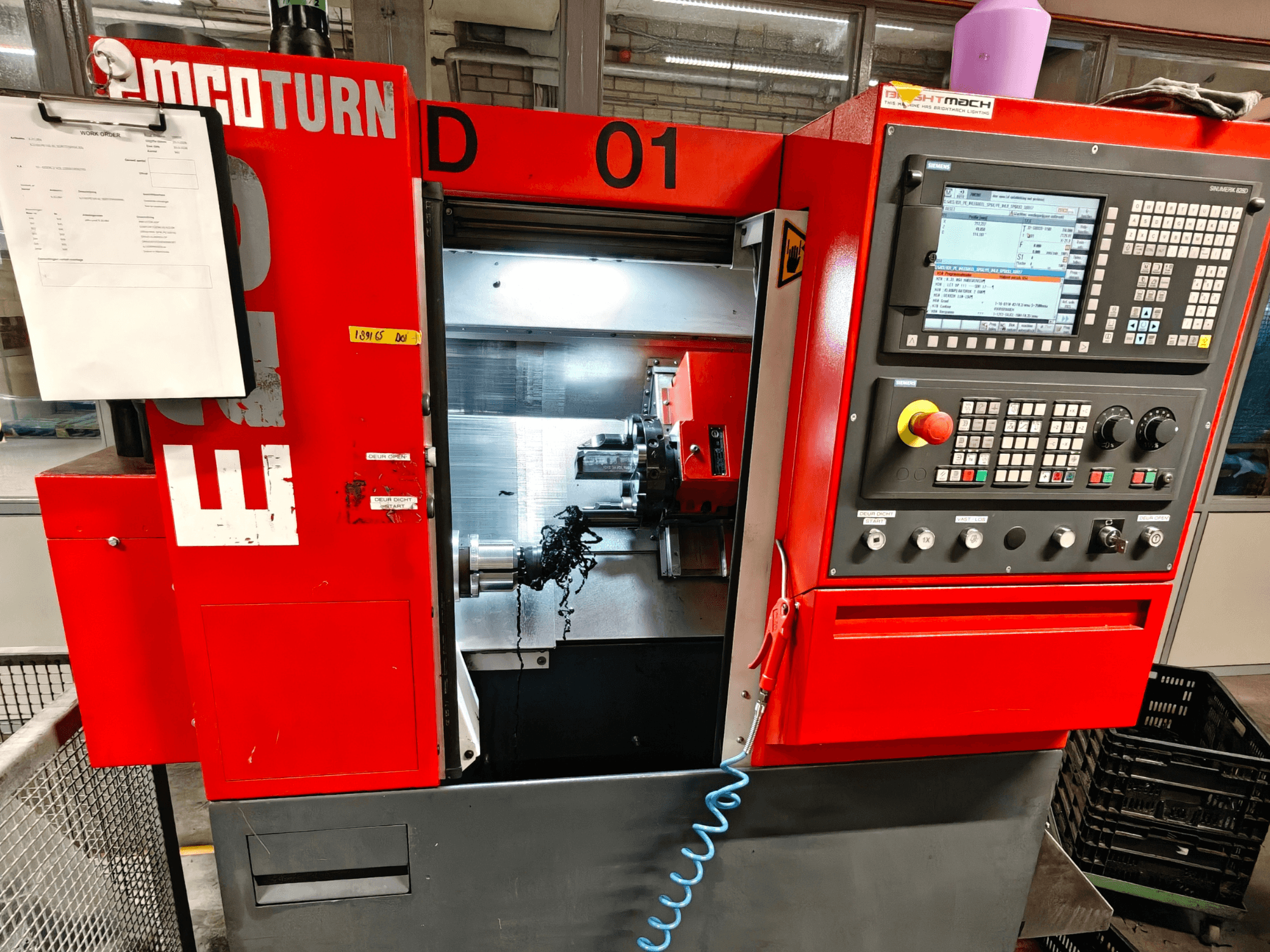 Prednji pogled na horizontalni tokarski stroj EMCO TURN E25, s upravljačkim elementima, držačem alata i radnim područjem s strugotinom.