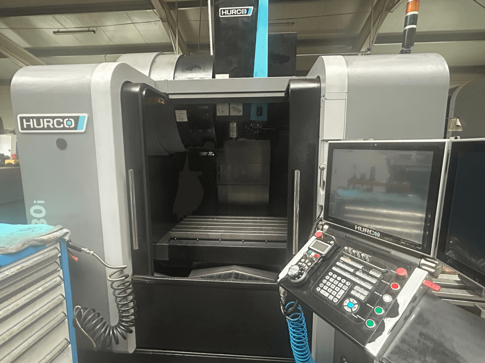 Prednji pogled na Hurco VM30i CNC stroj, s upravljačkom pločom s gumbima, zaslonom i prostorom za pohranu alata.