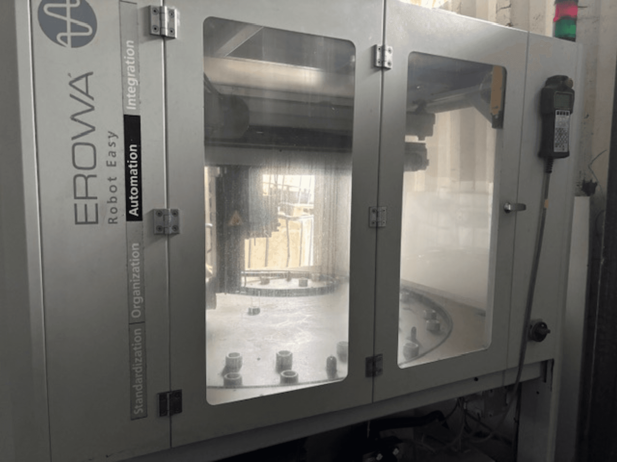 Prednji pogled na EROWA Robot Easy Automation; ima prozirna vrata, vidljive komponente automatizacije i upravljačku ploču.