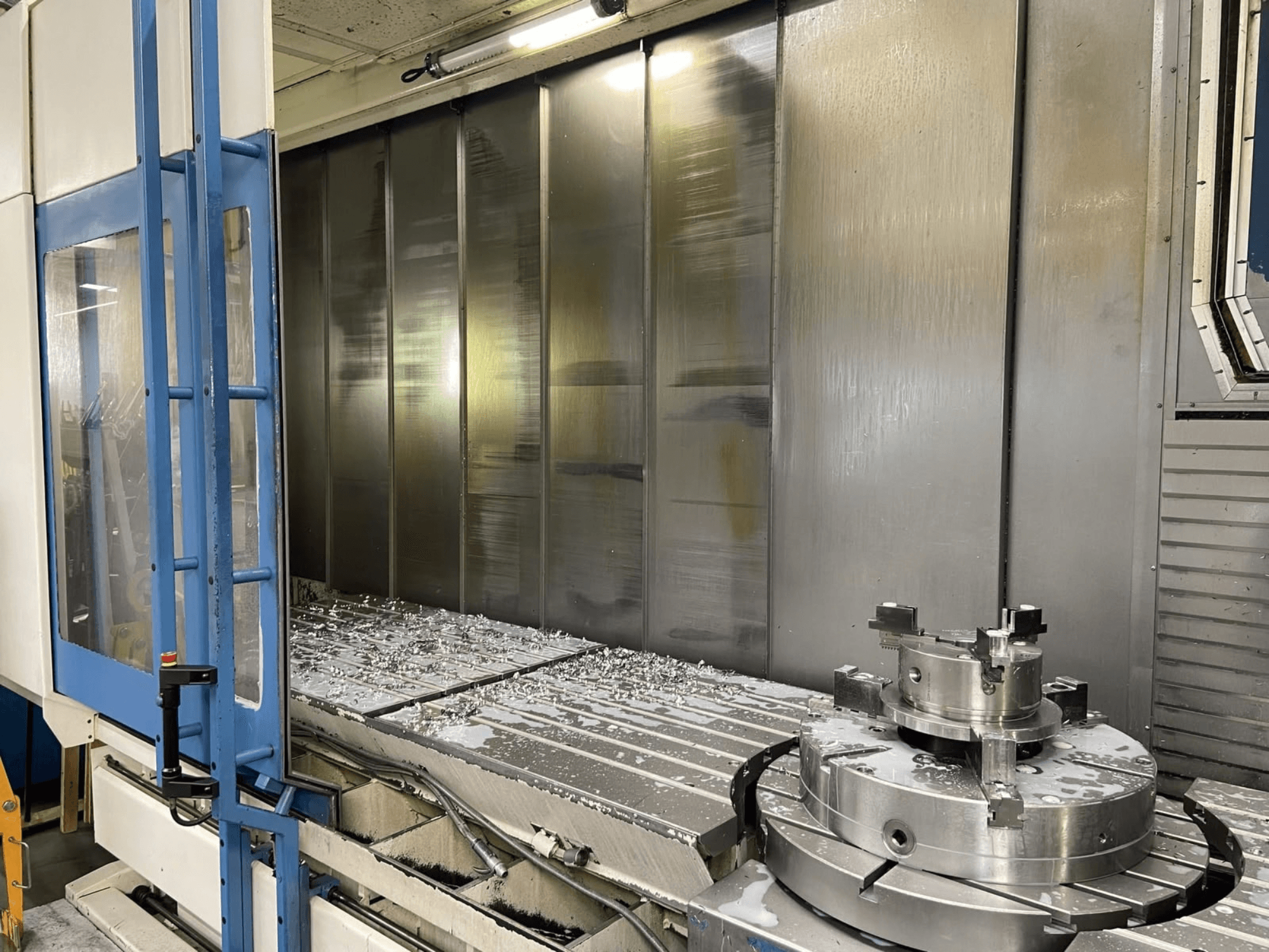 Vertikalni obradni centar AXA VHC-3-3000-M/E, prednji pogled, prikazuje strugotine glodanog metala na radnom stolu i alate za rezanje.