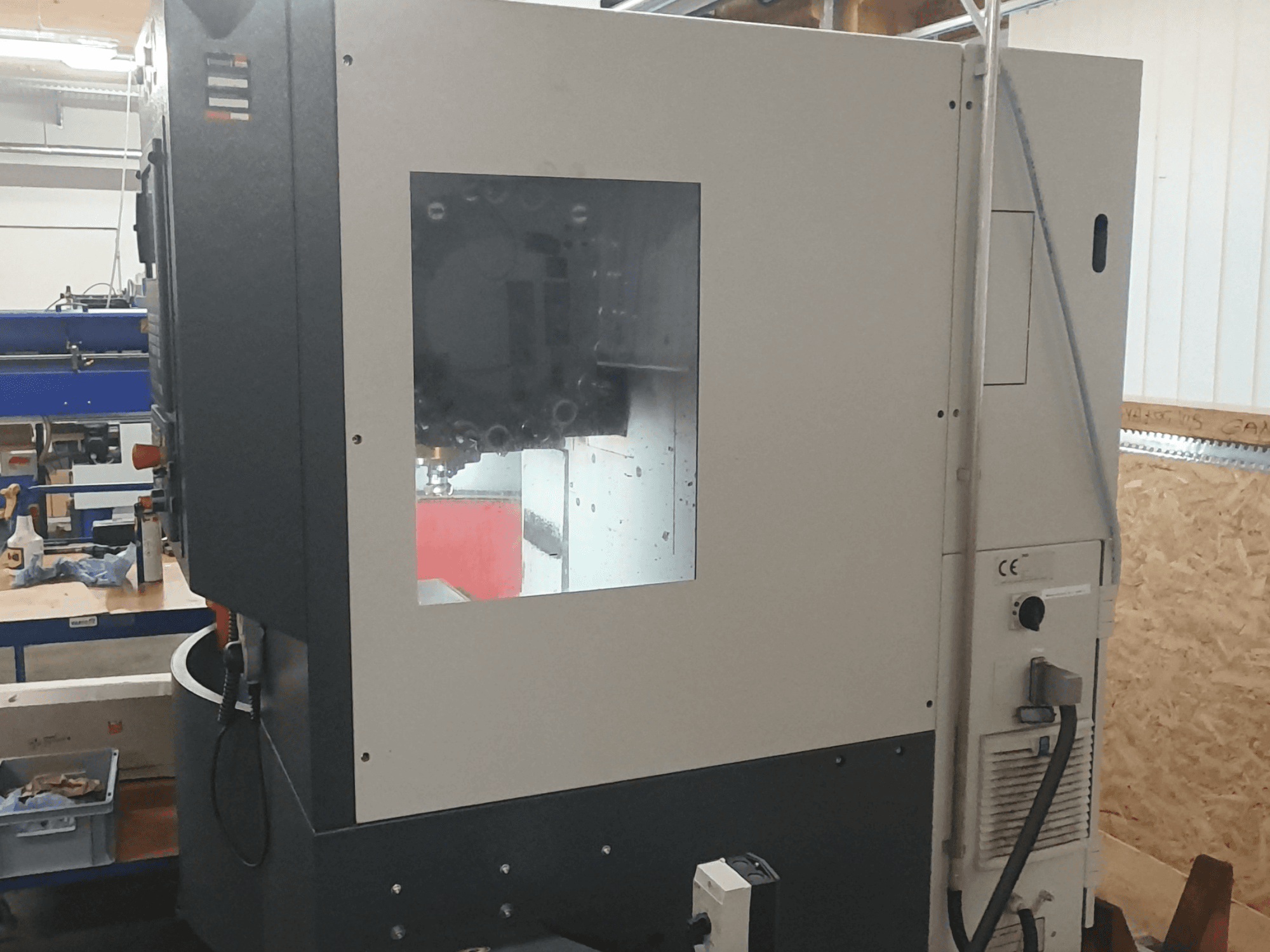 Bočni pogled na stroj za obradu metala s vidljivom upravljačkom pločom, velikim prozorom za pregled i složenim unutarnjim komponentama.