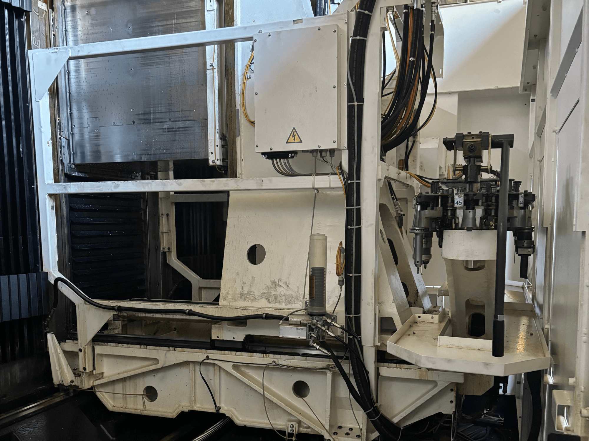 Bočni pogled industrijskog stroja koji prikazuje bijelu CNC glodalicu s vidljivim alatima, cijevima i upravljačkom pločom.