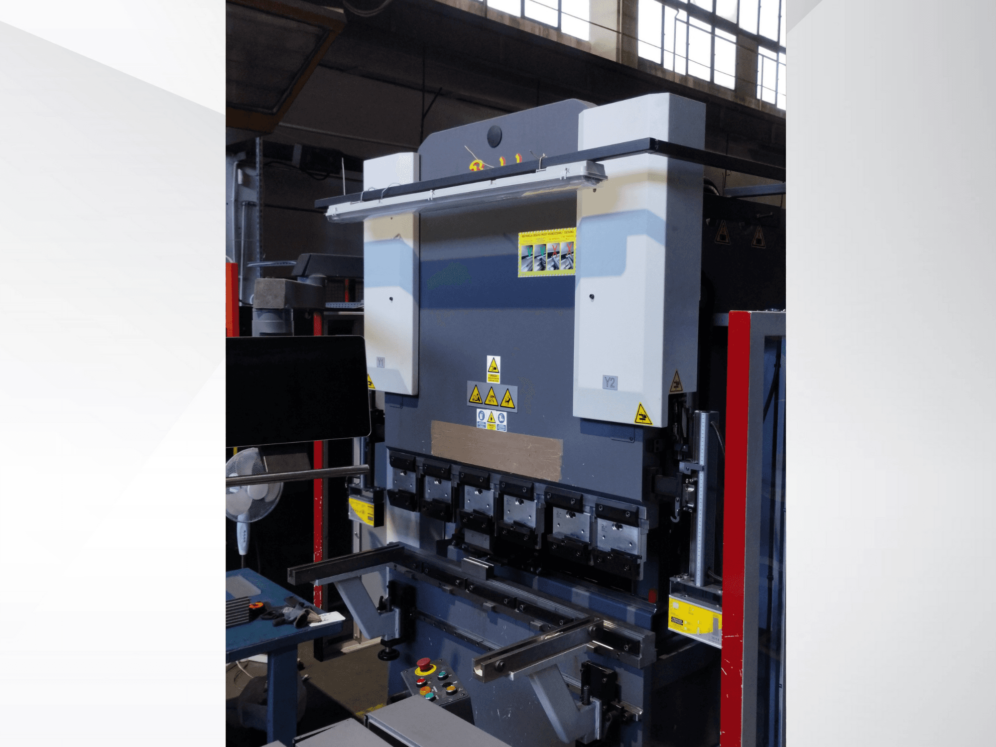 Stroj za savijanje preše, prednji pogled. Ima vidljive kontrole, sigurnosne naljepnice i više držača matrica za precizno savijanje.