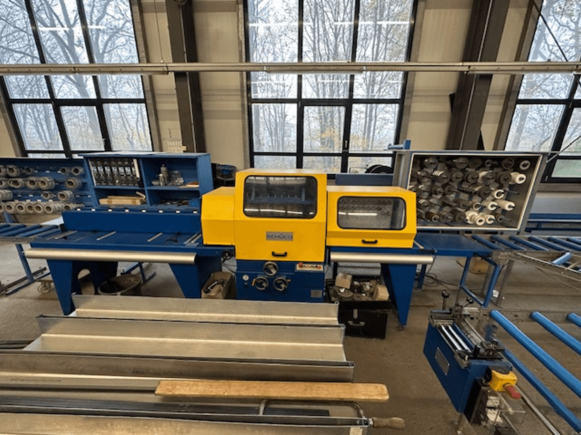 Prednji pogled na alatni stroj SCHÜCO ISOMAT 4, sa žutom upravljačkom pločom, više valjaka i pretincem za pohranu.