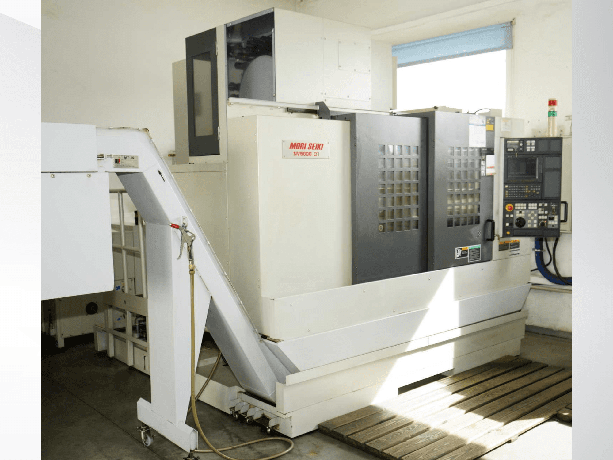 Vertikalni obradni centar MORI SEIKI NV 5000 alpha1 u prednjem pogledu, s prikazom upravljačke ploče, sigurnosnih značajki i prostora za utovar.