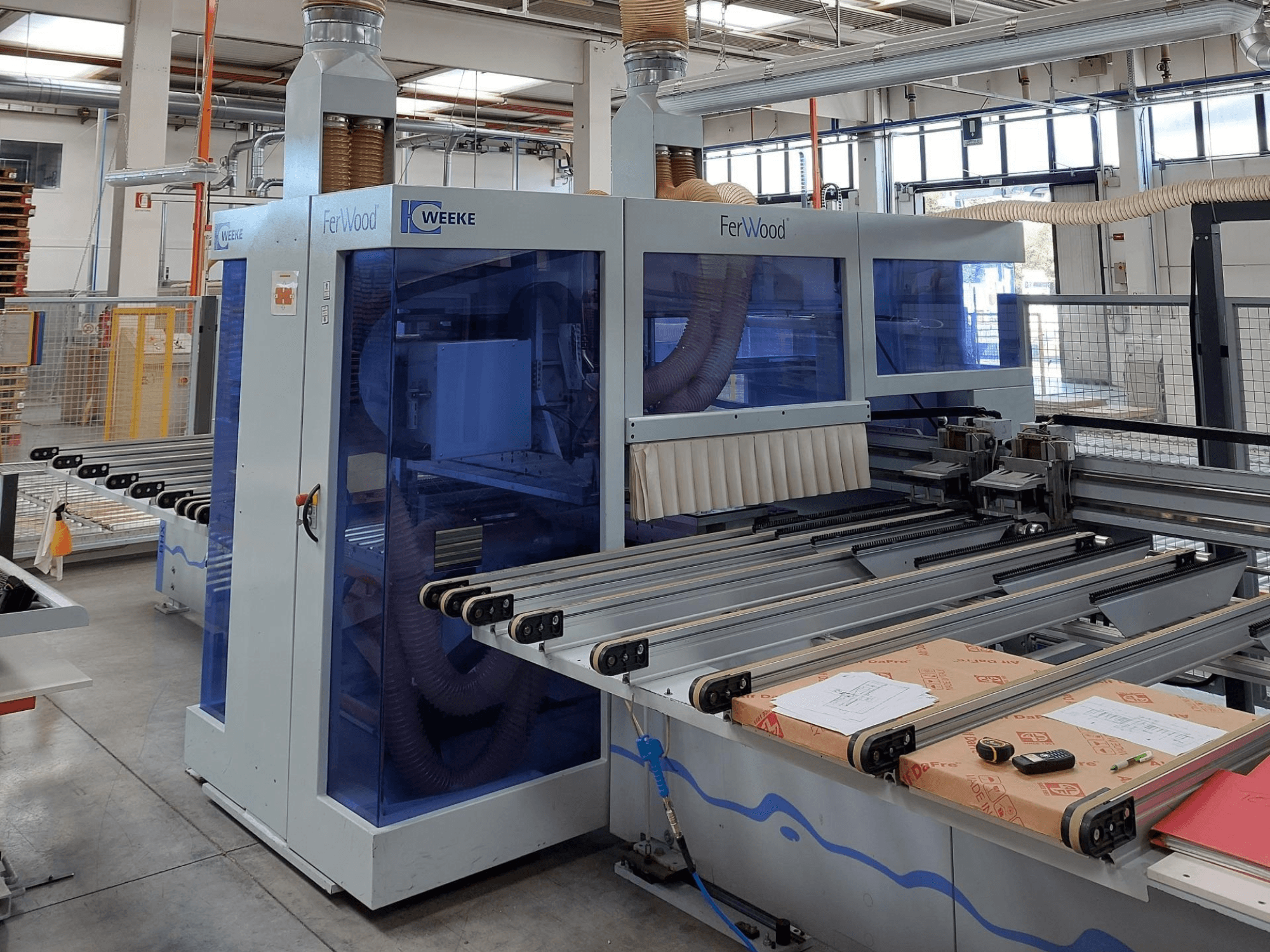 Weeke FerWood CNC stroj u radionici, prednji pogled koji prikazuje plavo obojene ploče, kontrolne tipke i radni stol s materijalima.