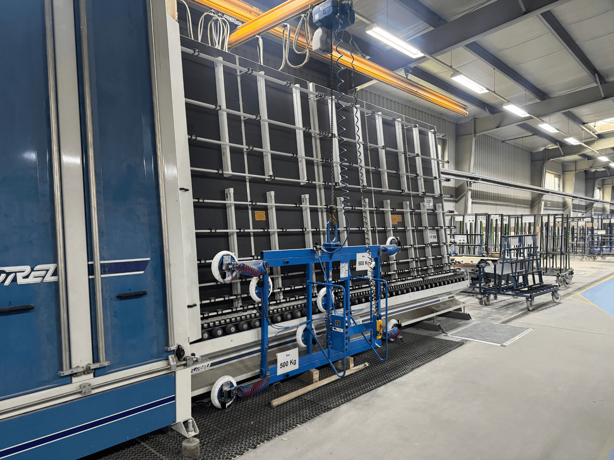 Industrijska oprema tvrtke Drel, s velikim okvirom i mehanizmom za podizanje, prikazana sa strane u tvorničkom okruženju.