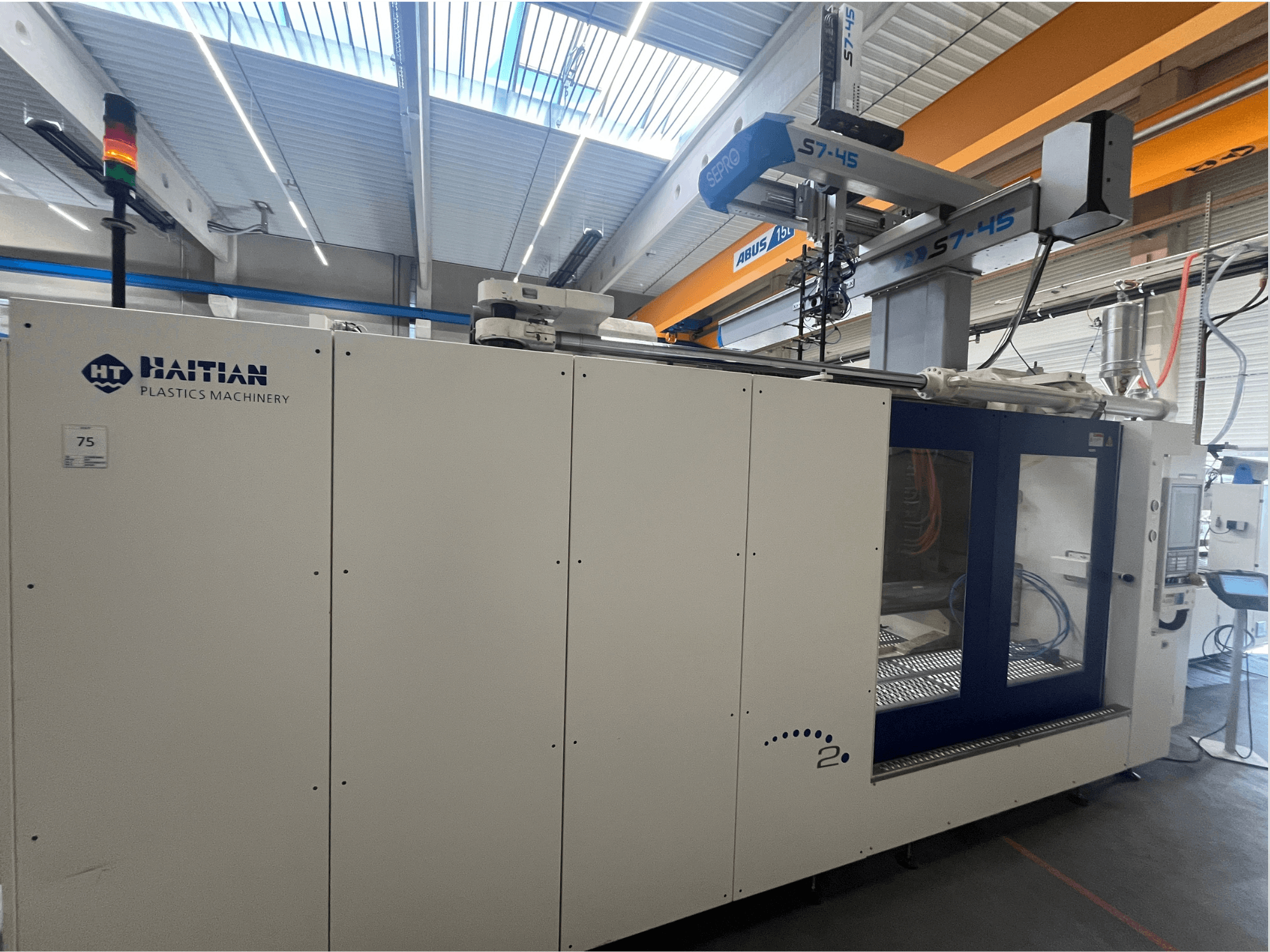 Bočni pogled na haićanski stroj za brizganje plastike S7-45 s upravljačkom pločom i sigurnosnim svjetlosnim indikatorom. Bijelo-plavi dizajn.