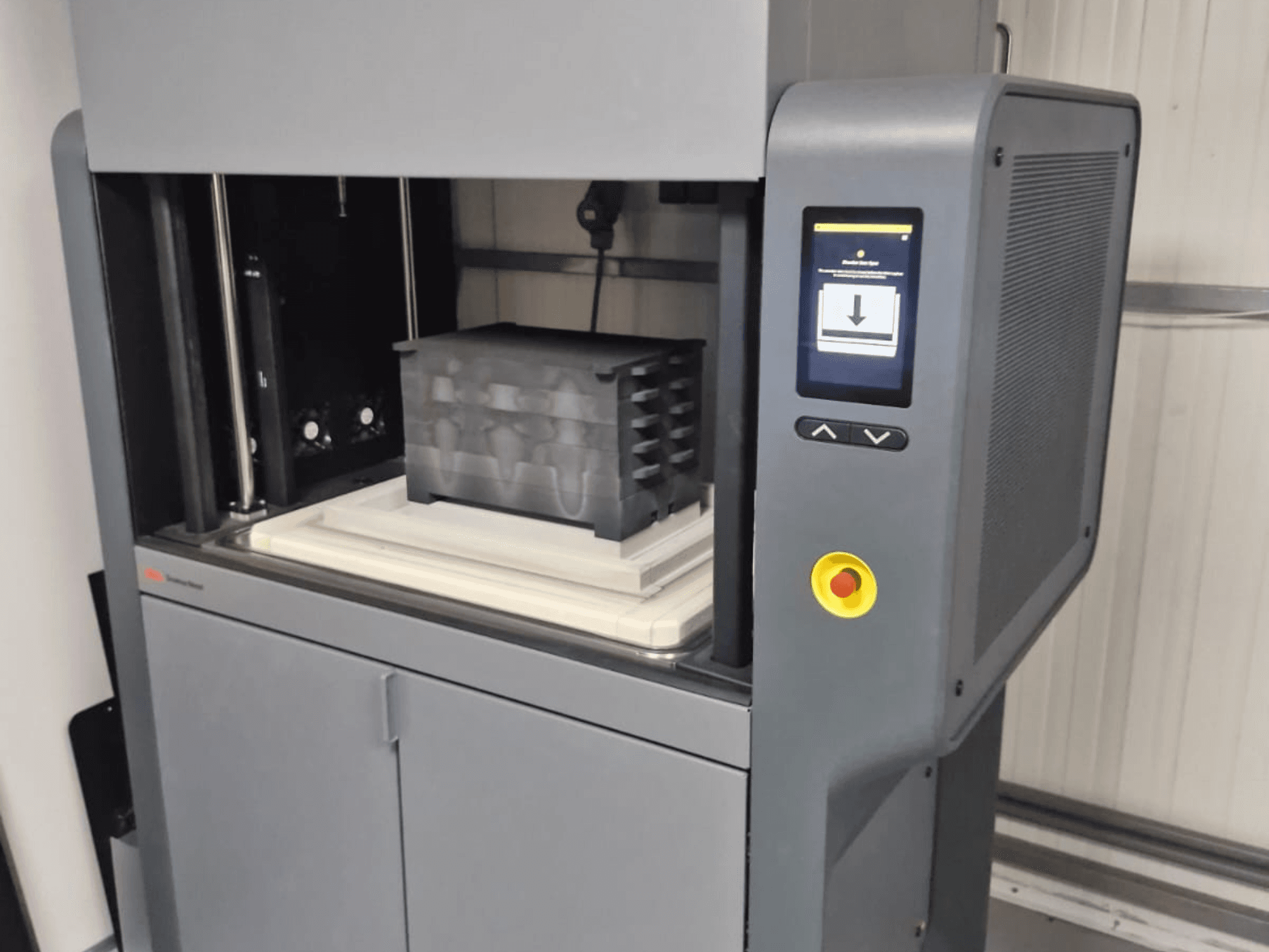 3D printer Metal Studio 2 tvrtke Desktop Metal, prednji pogled koji prikazuje upravljačku ploču i podlogu za ispis s crnim spremnikom.