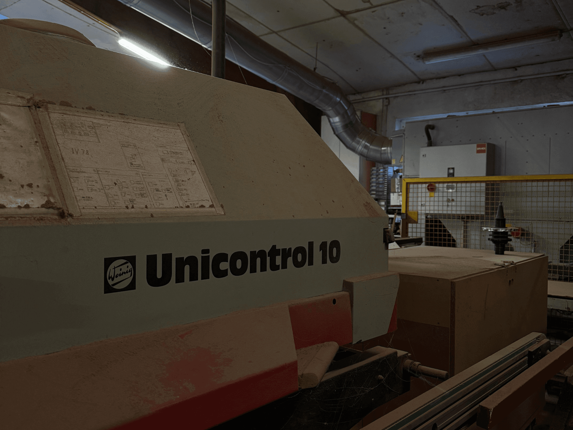 Stroj Weinig Unicontrol 10 gledan iz bočnog kuta, prašnjava površina, tehničke sheme vidljive na prednjoj ploči.