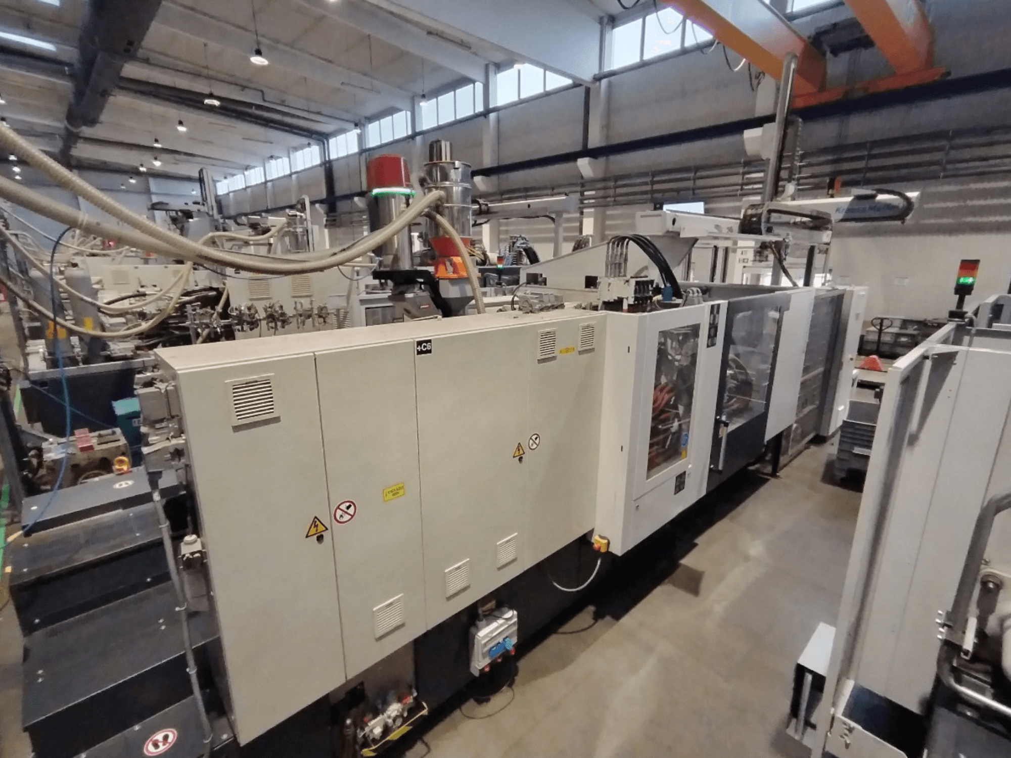 Industrijski stroj za brizganje plastike prikazan s bočne strane, s upravljačkom pločom i sigurnosnim upozorenjima. Marka: Nepoznata.