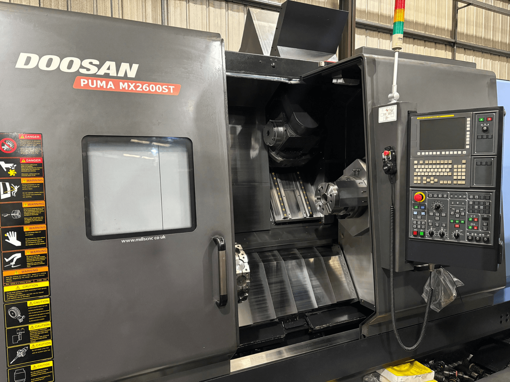 Doosan PUMA MX2600ST CNC tokarski stroj, prednji pogled, prikazuje upravljačku ploču, vreteno i područje obrade s vidljivim sigurnosnim upozorenjima.