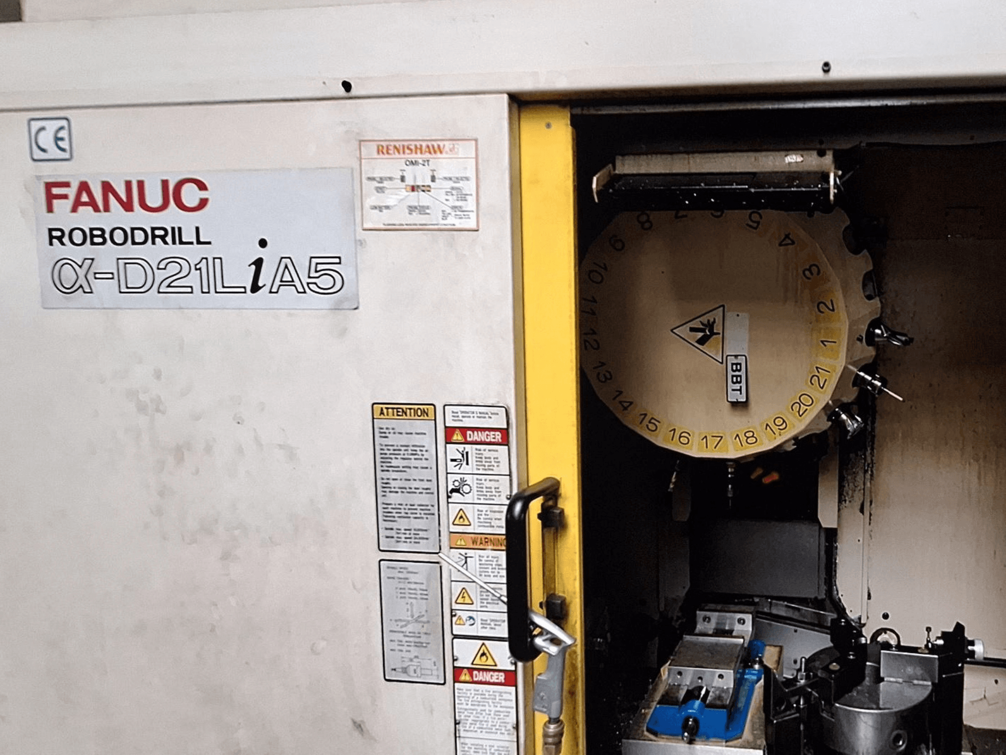 FANUC Robodrill α-D21LiA5, prednji pogled. Prikazuje vrtuljak alata i područje obrade sa stezaljkama i upozorenjima na vratima.