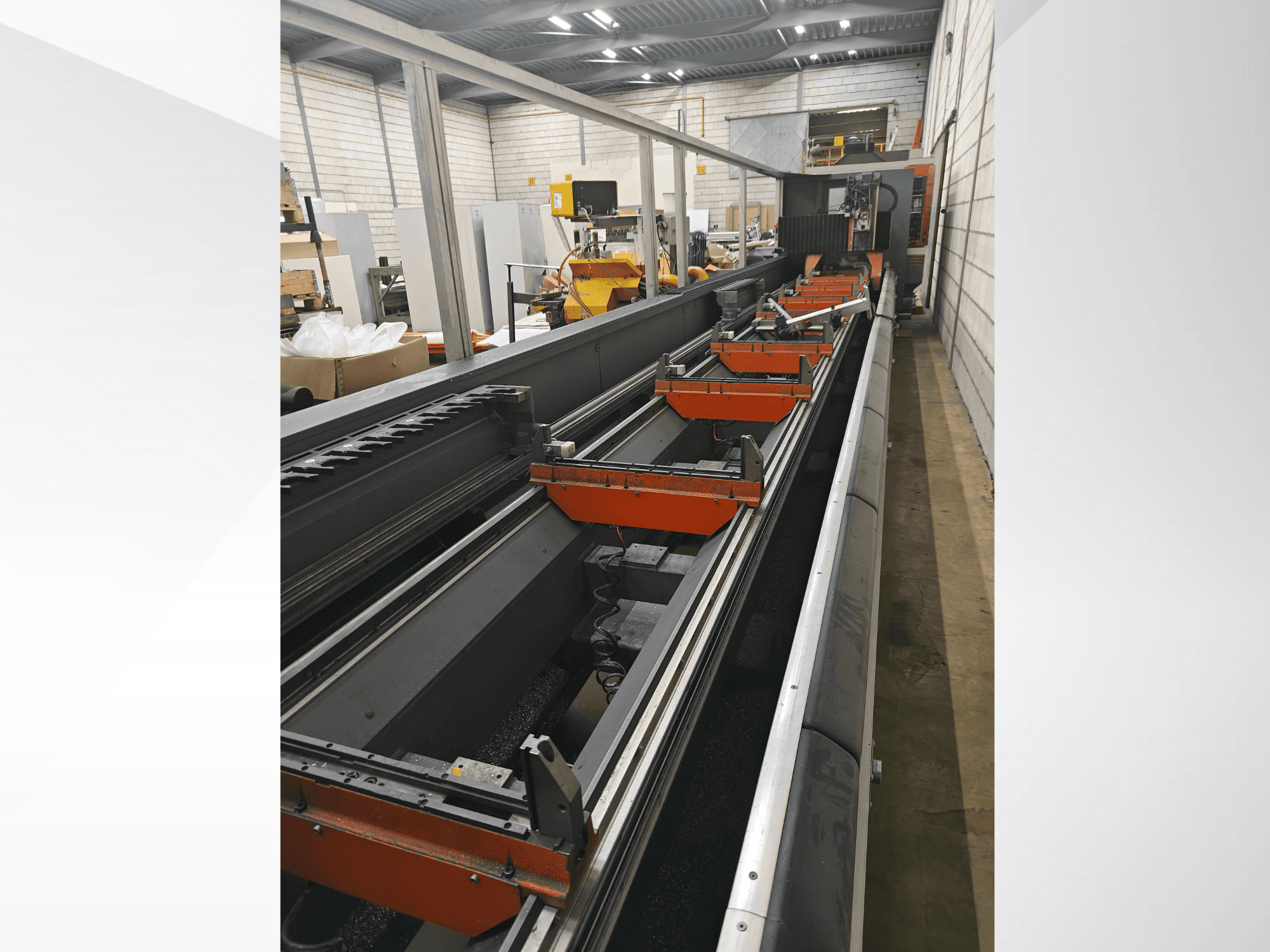 Bočni pogled na industrijski CNC stroj s linearnim vodilicama, narančastim stezaljkama i preciznim komponentama u skladišnom okruženju.