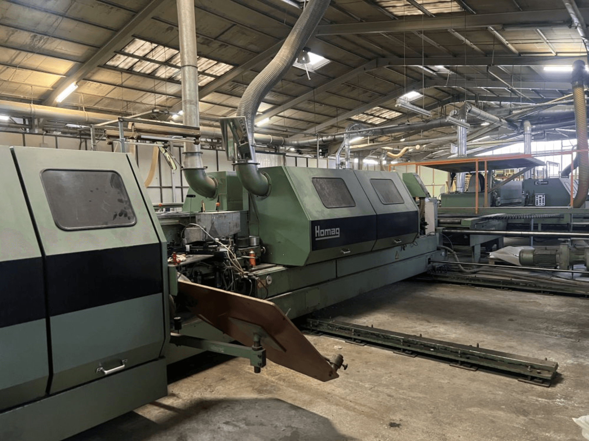 Homag industrijski stroj u zelenoj boji, bočni pogled, s vidljivim operativnim komponentama i upravljačkom pločom u skladišnom okruženju.