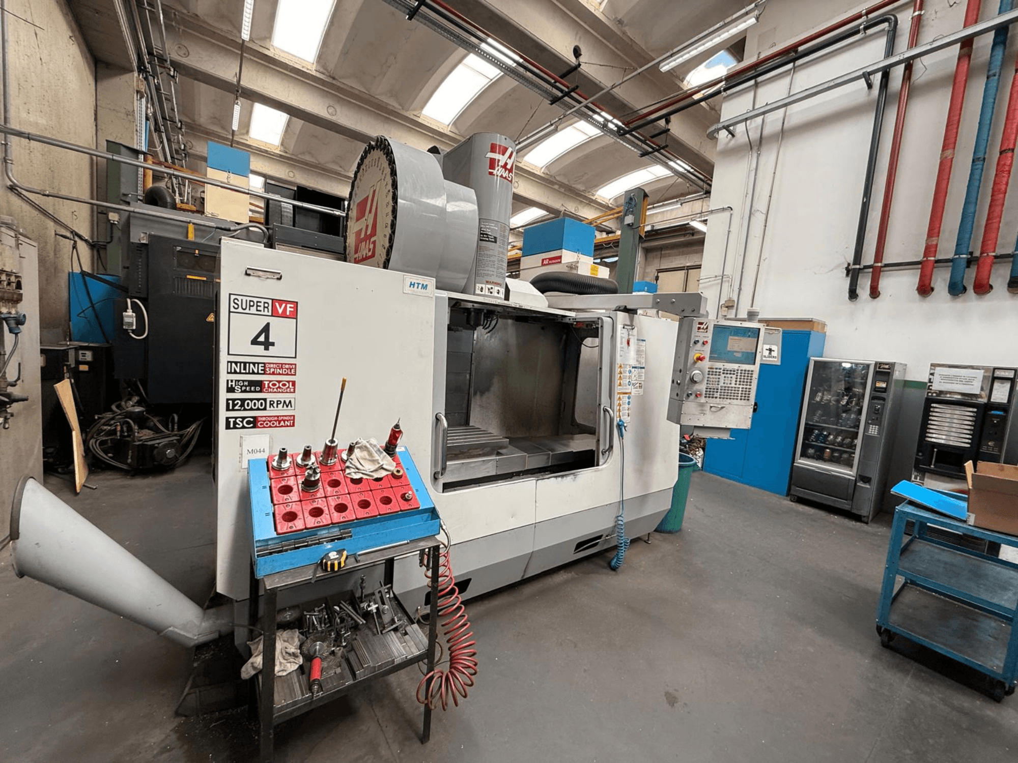 HAAS Super VF 4 CNC glodalica s upravljačkom pločom, vretenom od 12 000 okretaja u minuti i alatima na plavom stalku za odlaganje, bočni pogled.