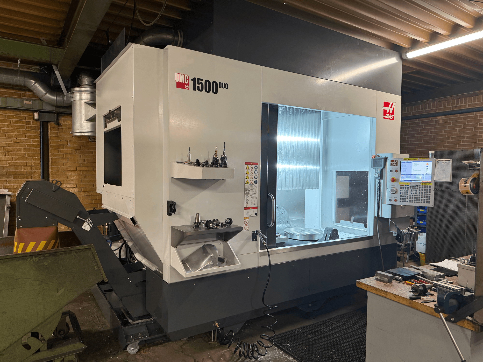 Haas UMC 1500DUO CNC stroj, pogled sprijeda, ima veliki prozor, upravljačku ploču i držače alata na polici.