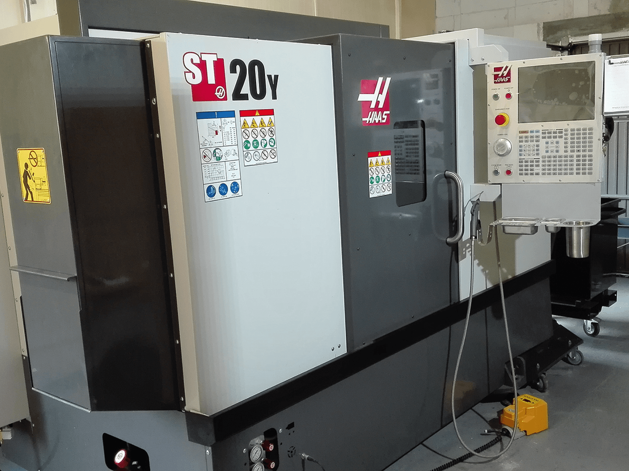 Haas ST20Y CNC tokarilica u prednjem pogledu, s upravljačkom pločom, sigurnosnim naljepnicama i sustavom rashladnog sredstva.