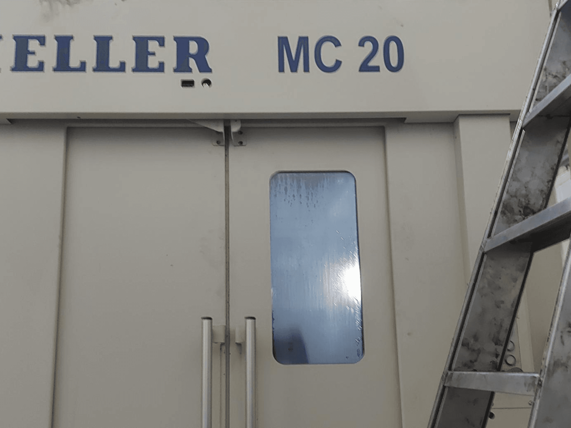 Prednji pogled na horizontalni obradni centar HELLER MC 20, s kvakama na vratima i malim prozorom. Ljestve sa strane.