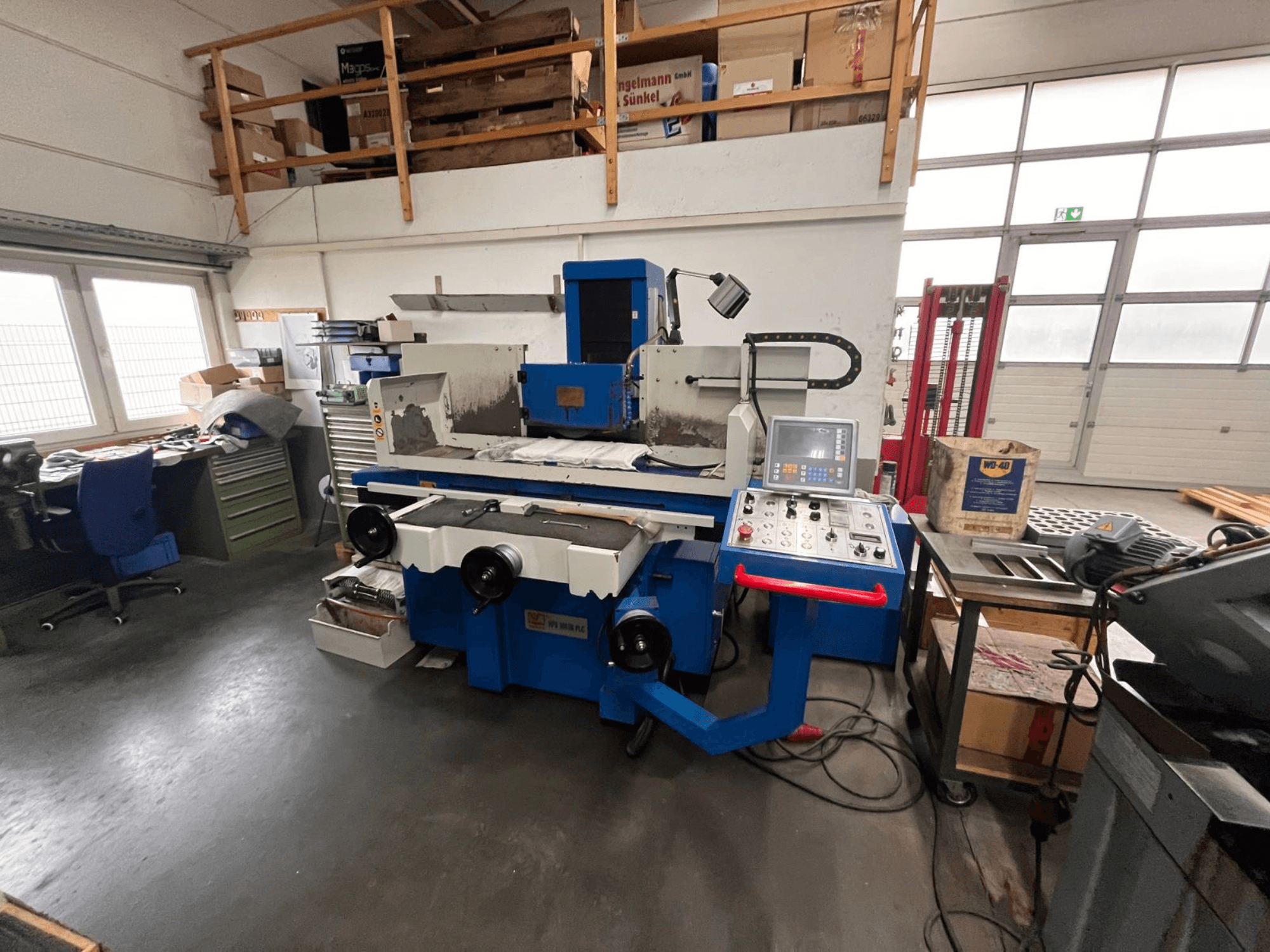 Plava brusilica za površine s digitalnom upravljačkom pločom, prednji pogled, prikazuje nered u radnom prostoru i zeleni ormarić za alat.