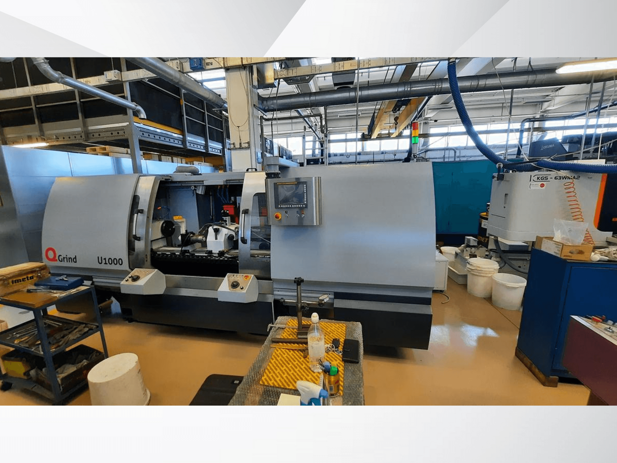 Stroj Q-Grind U1000 u radionici, s prednjim pogledom na upravljačku ploču i otvoreni prostor za rezanje, okružen opremom.