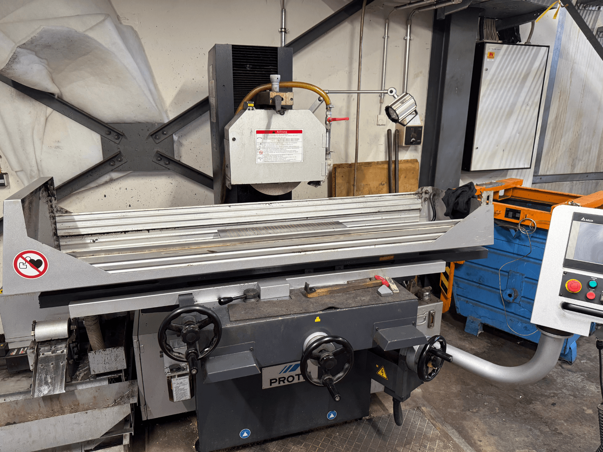 PROTEC stroj, prednji pogled, prikazuje površinsku brusilicu s ručnim kontrolama, sigurnosnim upozorenjima i sustavom hlađenja.