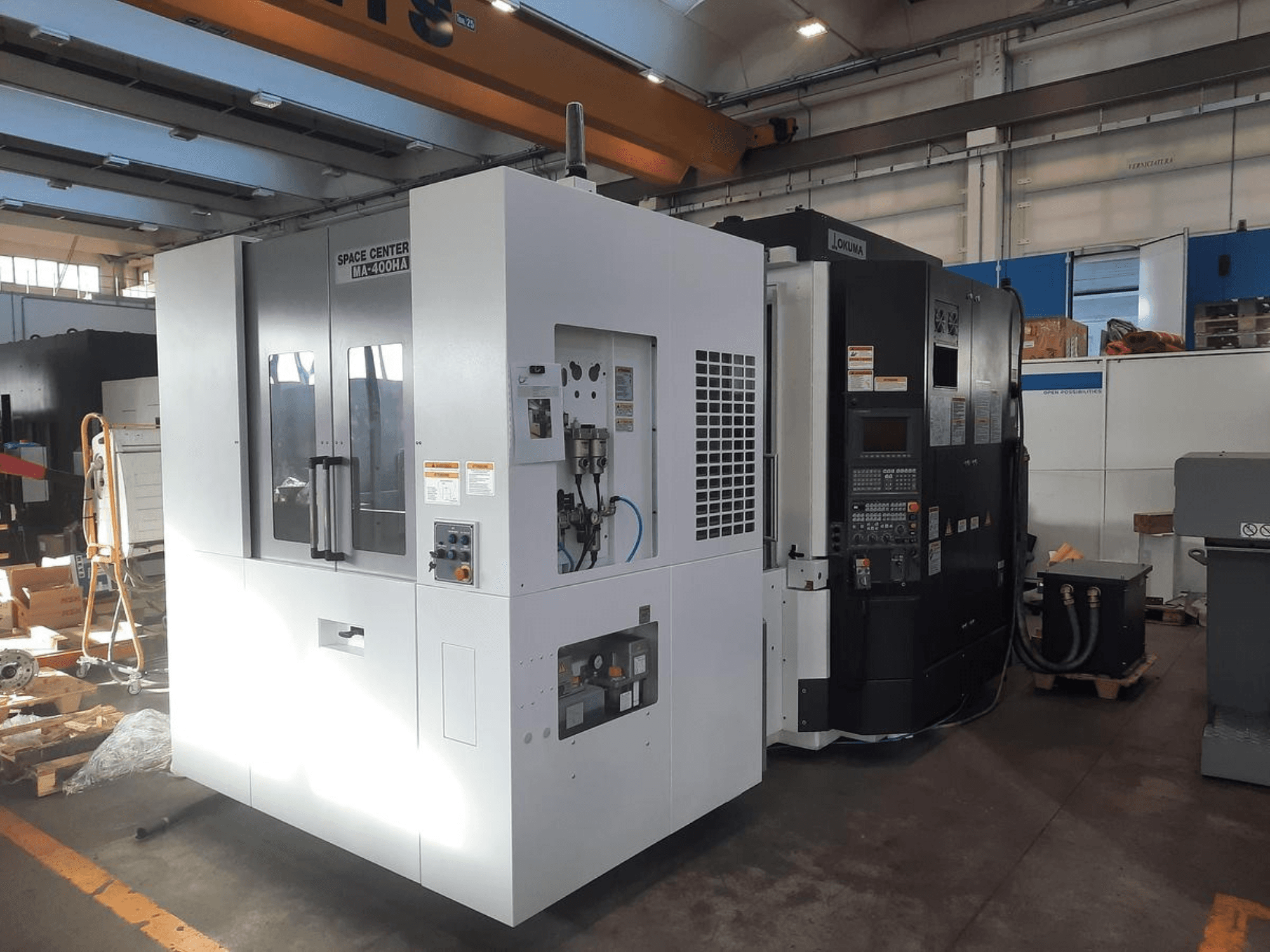 Prednji pogled na CNC strojeve SPACE CENTER IM-400HAA i OKUMA, s prikazom raznih kontrola i oznaka proizvođača.