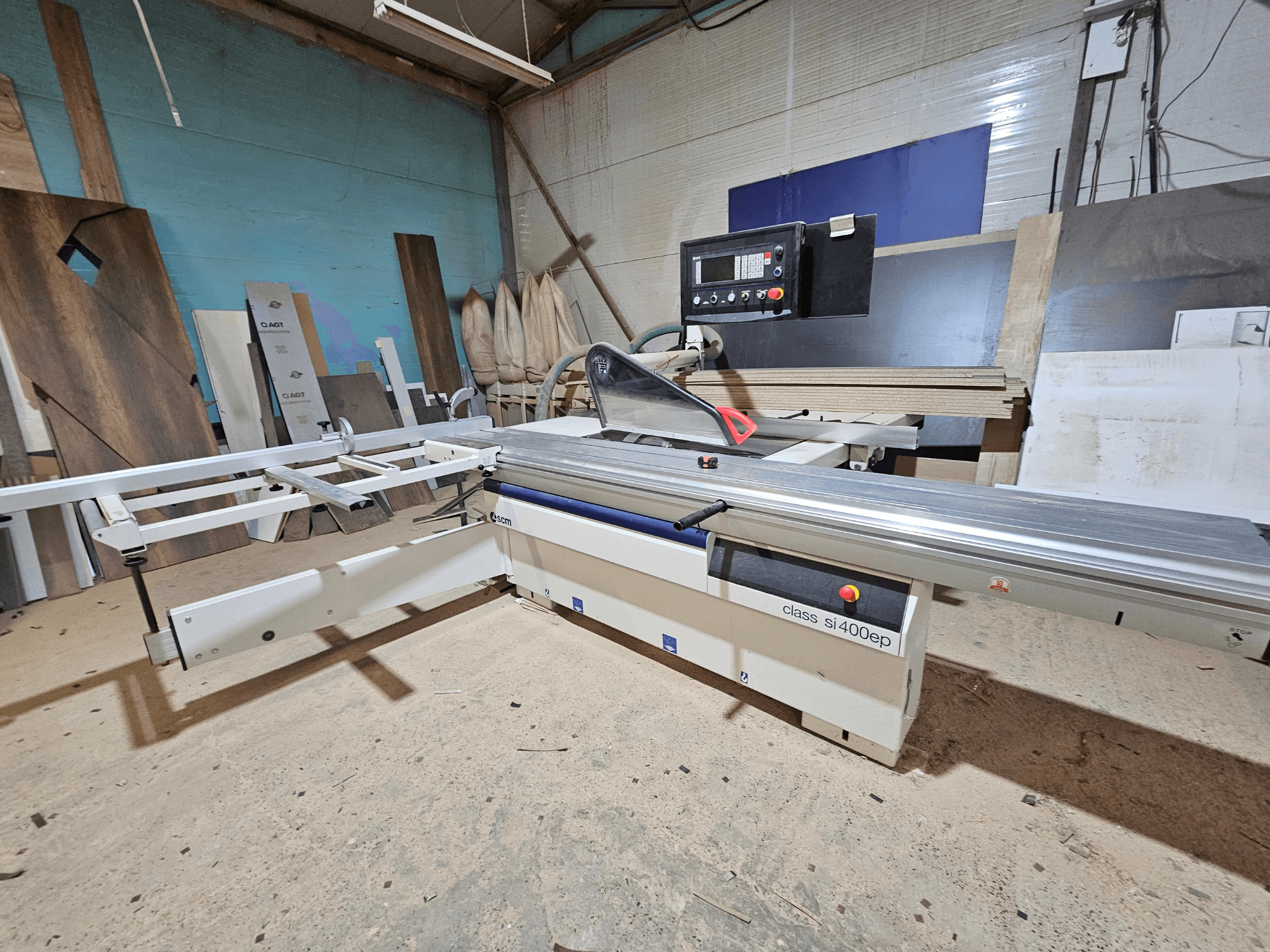 Panelna pila klase SI400EP, pogled sprijeda, s podesivom ogradom, postavljena na pjeskovitom podu radionice, okružena drvenim pločama.