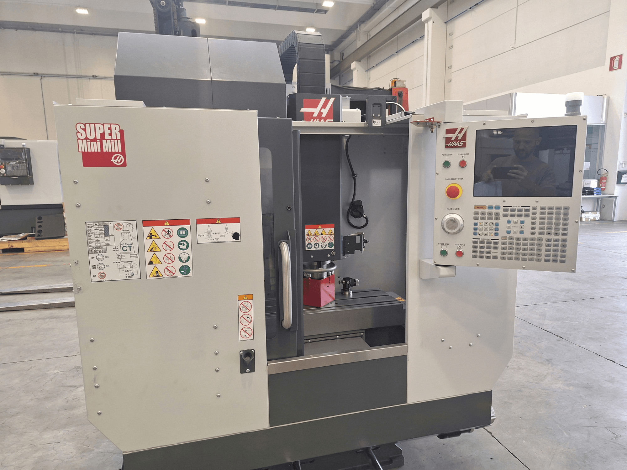 Prednji pogled na HAAS Super Mini Mill s upravljačkom pločom, sigurnosnim naljepnicama i područjem obrade s postavom obratka.