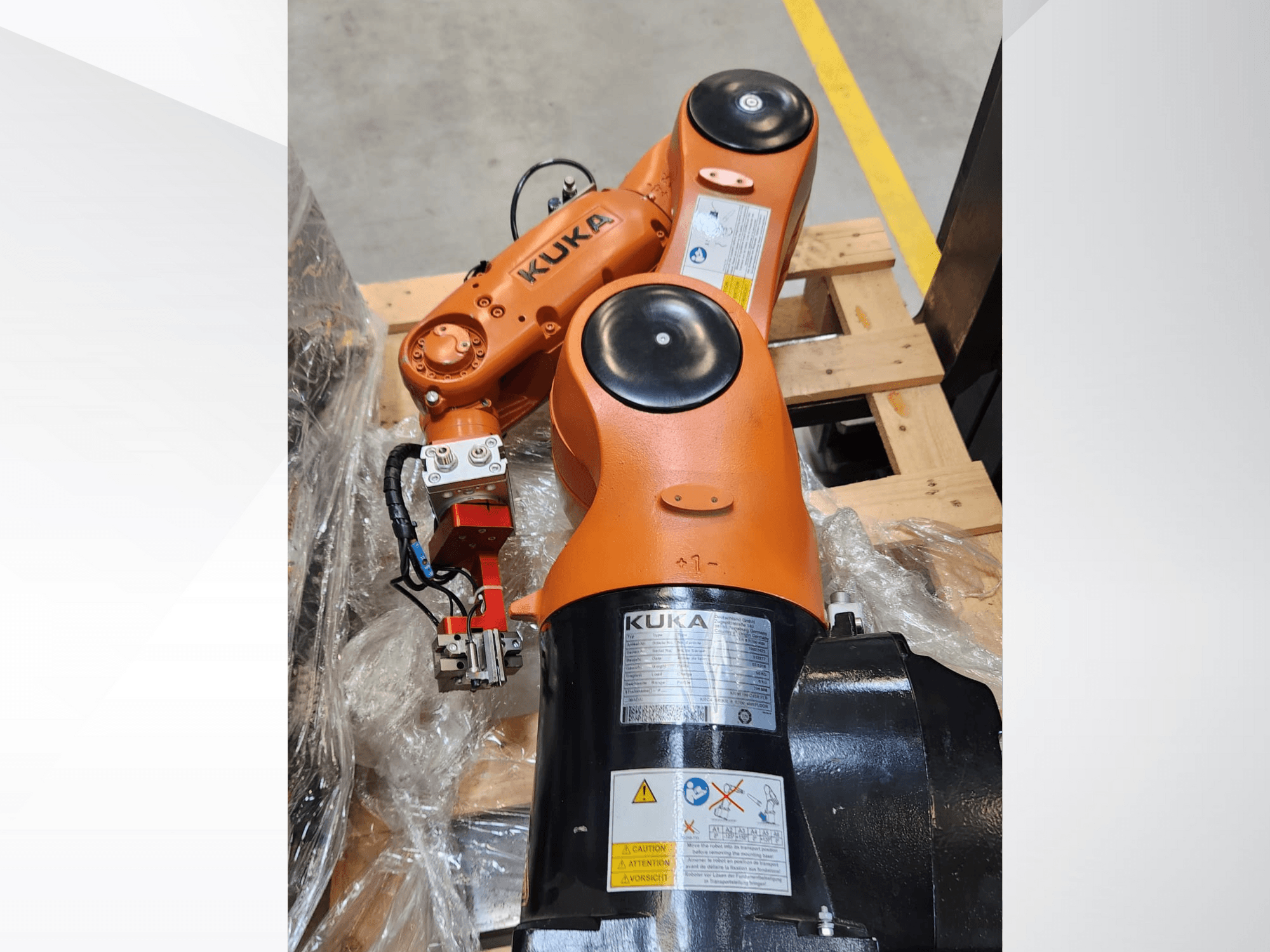KUKA robotska ruka s narančastom završnom obradom, bočni pogled, s hvataljkom i upravljačkim ožičenjem na drvenoj paleti.