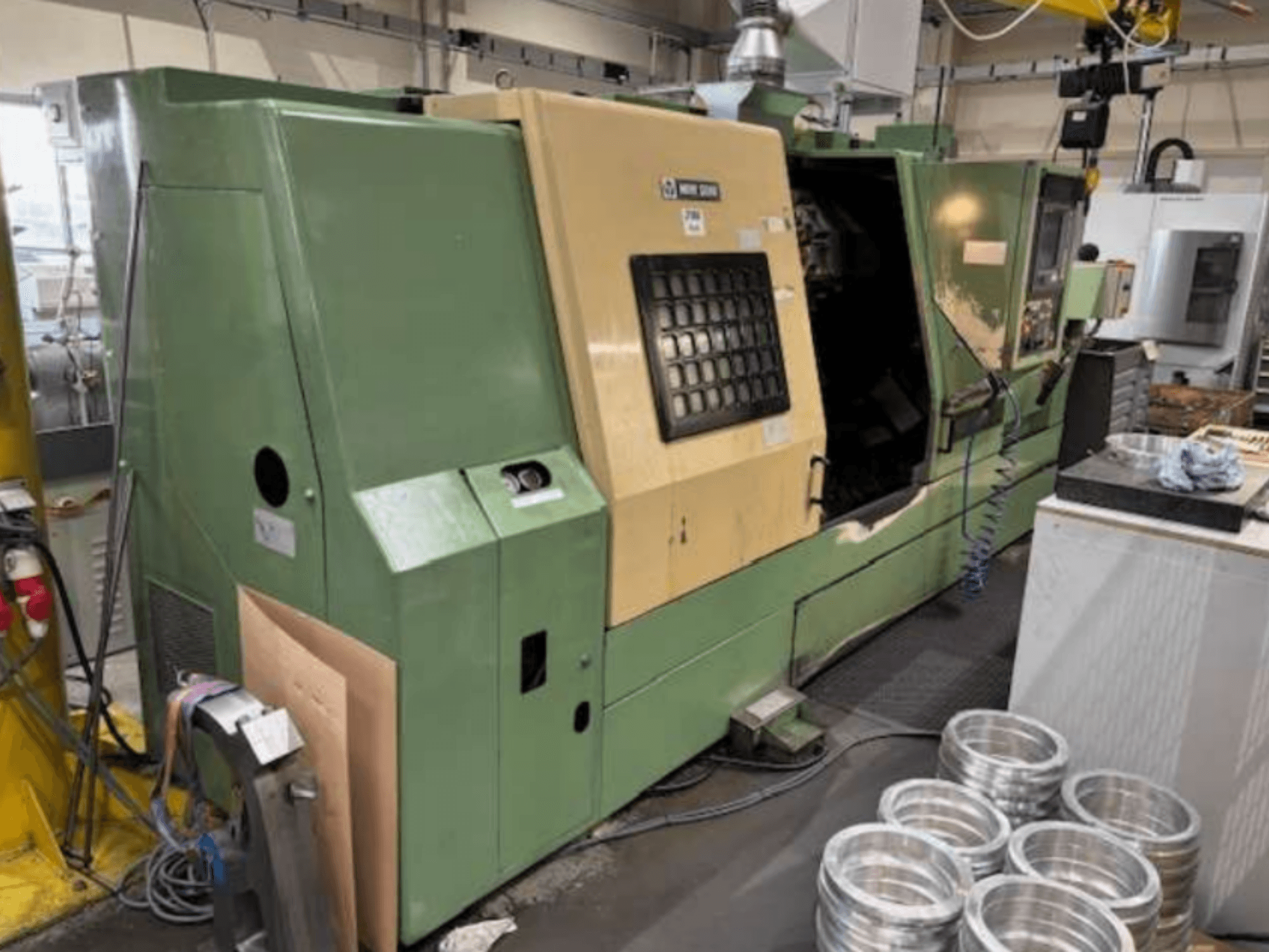 Zeleni CNC tokarski stroj tvrtke Mazak, pogled sprijeda, s upravljačkom pločom i obrađenim aluminijskim dijelovima na radnom stolu.