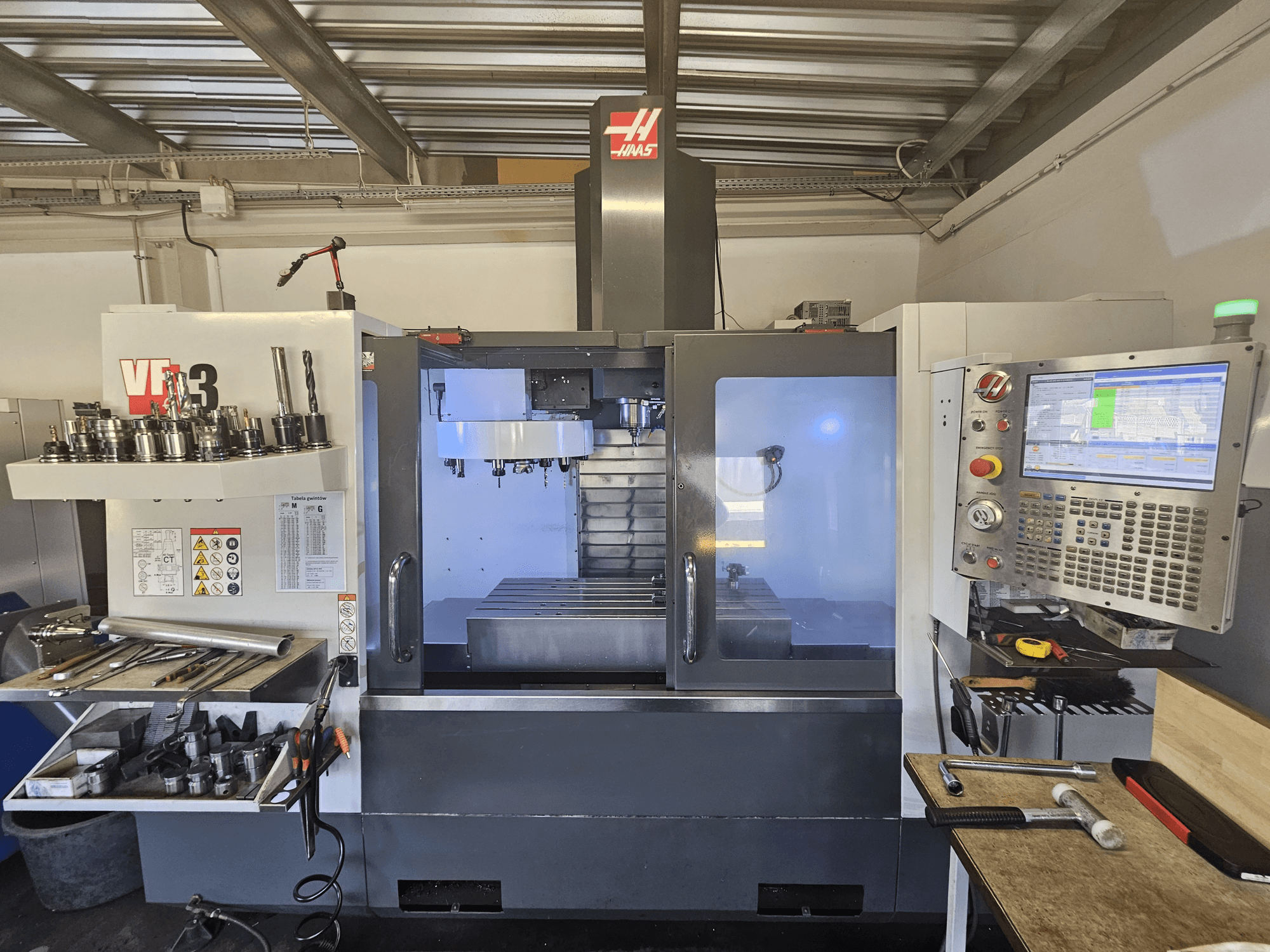 Haas VF-3 CNC stroj u radionici, prednji pogled s alatima, upravljačkim elementima i područjem za glodanje s osvijetljenom unutrašnjošću.