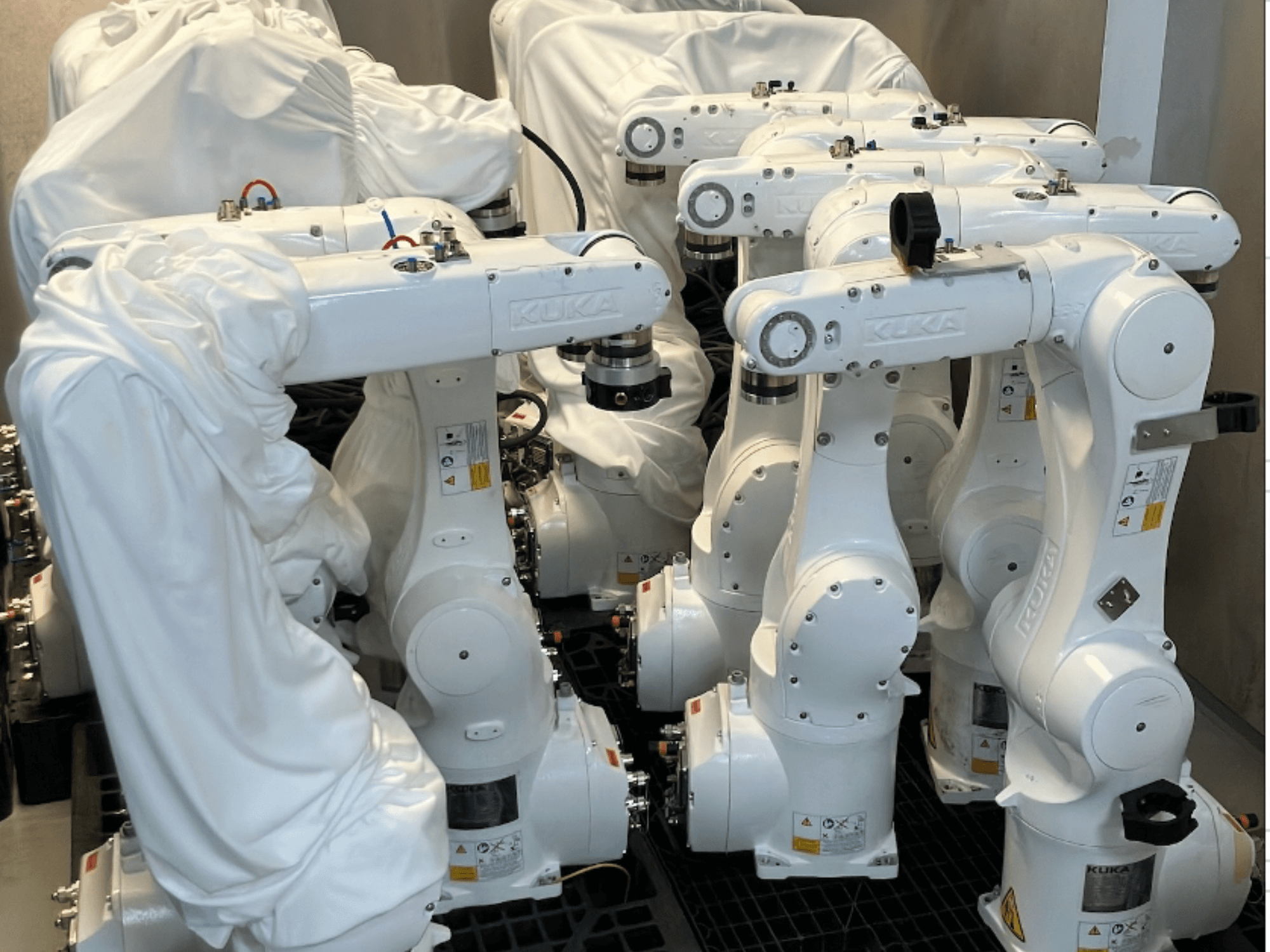 KUKA KR 10 R900-2 robotske ruke prekrivene bijelom tkaninom, gledane iz gornjeg kuta, prikazuju više jedinica u skladištu.