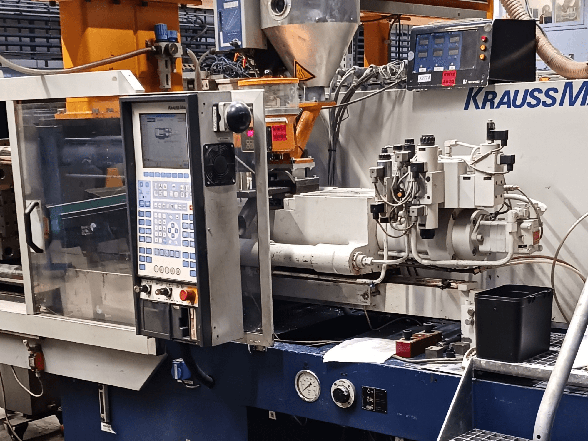 KraussMaffei stroj za brizganje plastike s upravljačkom pločom, hidrauličkim jedinicama i alatima u prvom planu, prednji pogled.